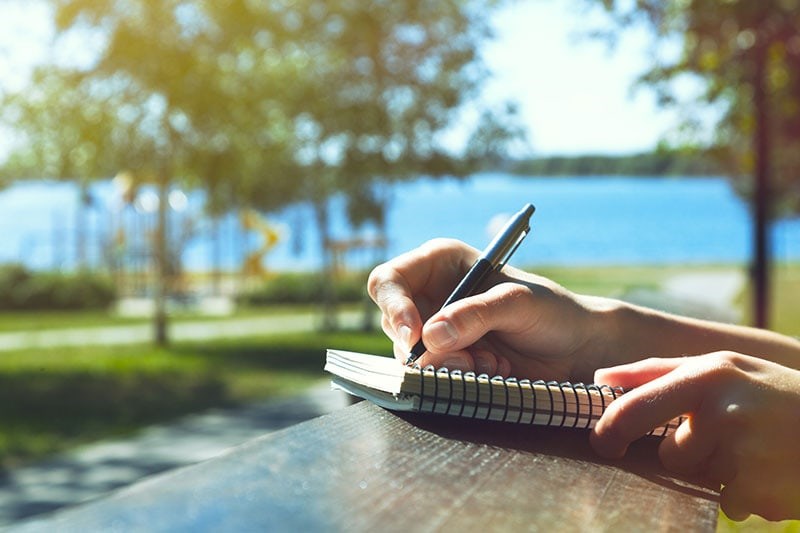 Unidentified person journaling by a lake with trees