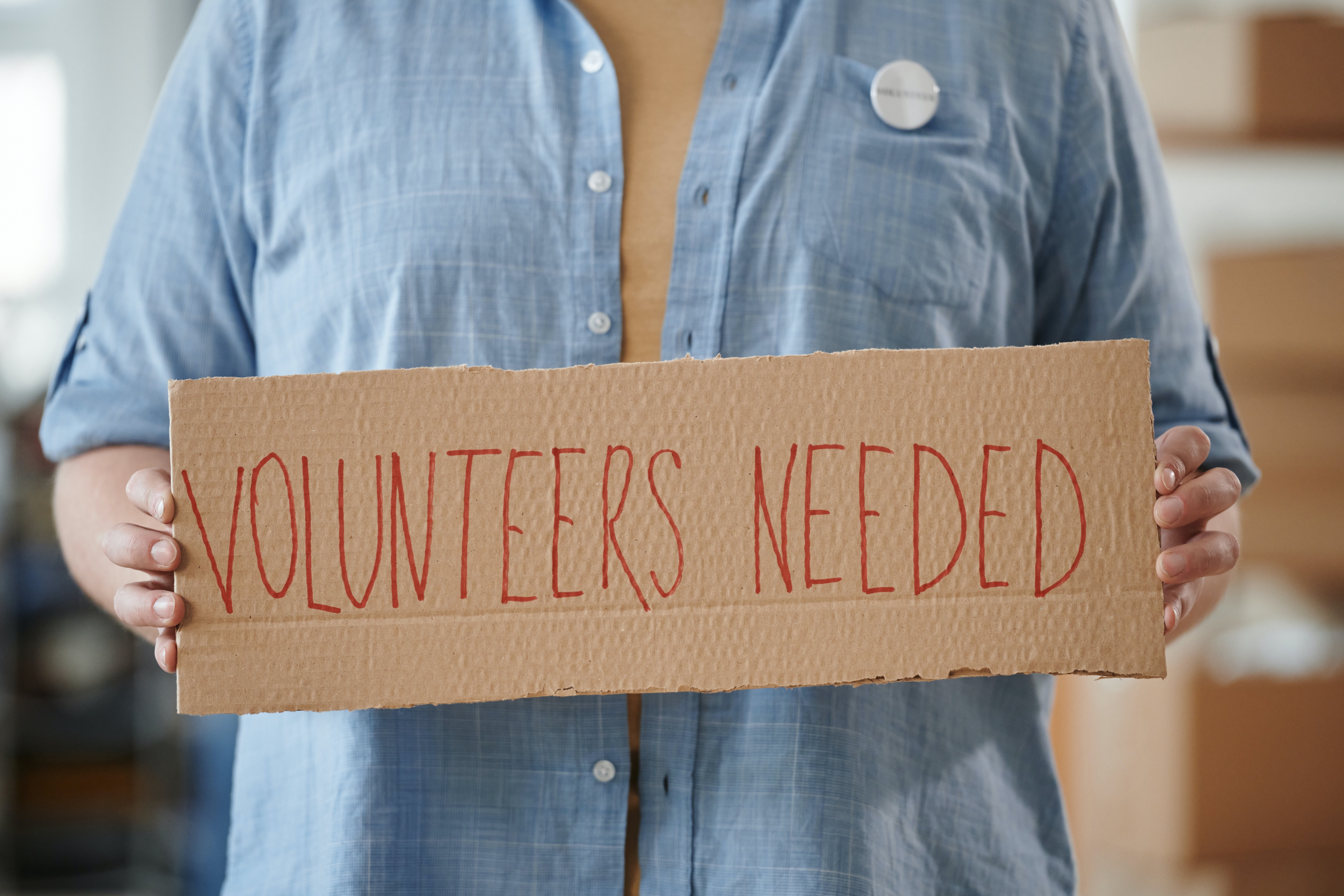 Person Holding a Volunteers Needed Sign