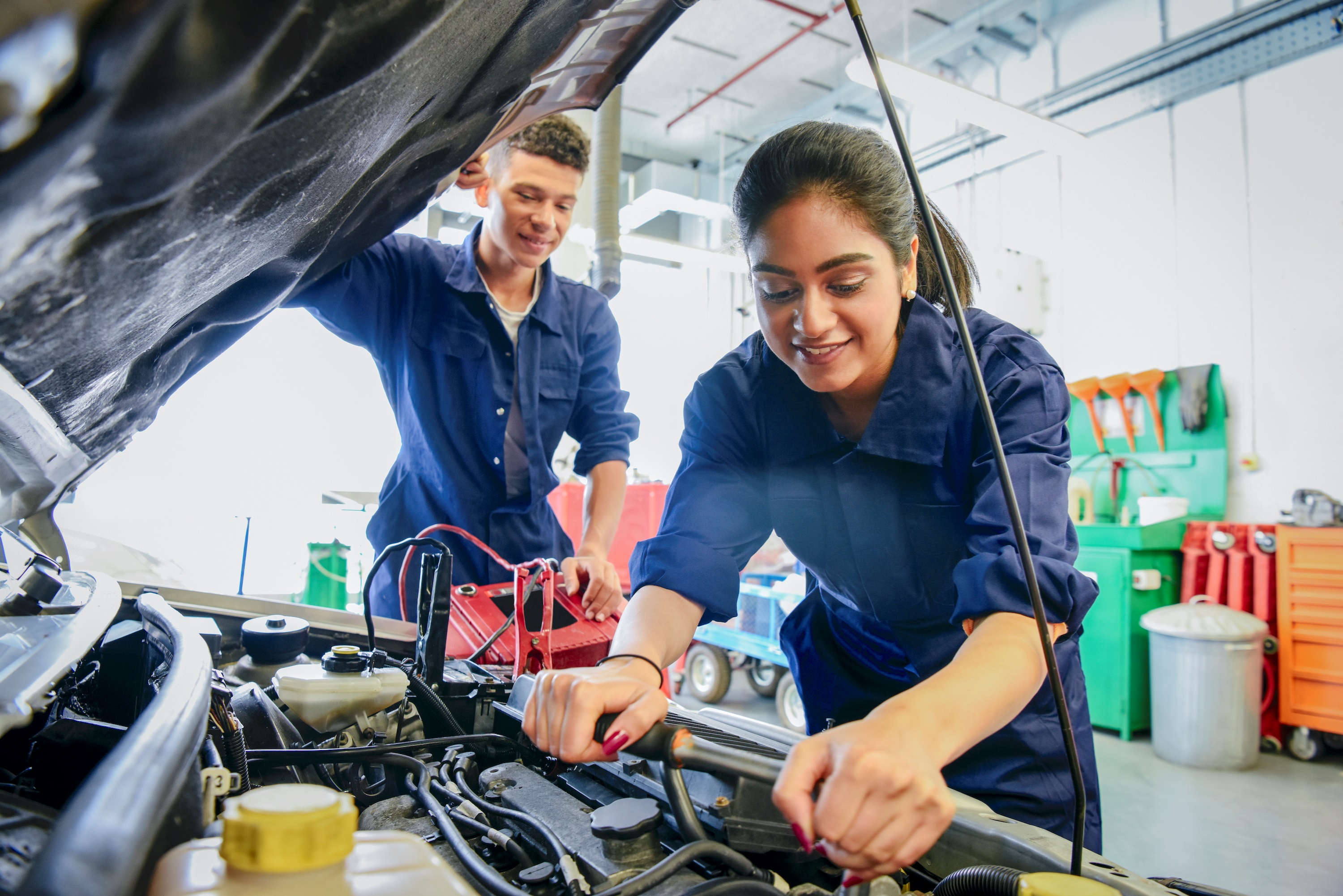 Two Car Mechanic Students Working on a Car in a Garage