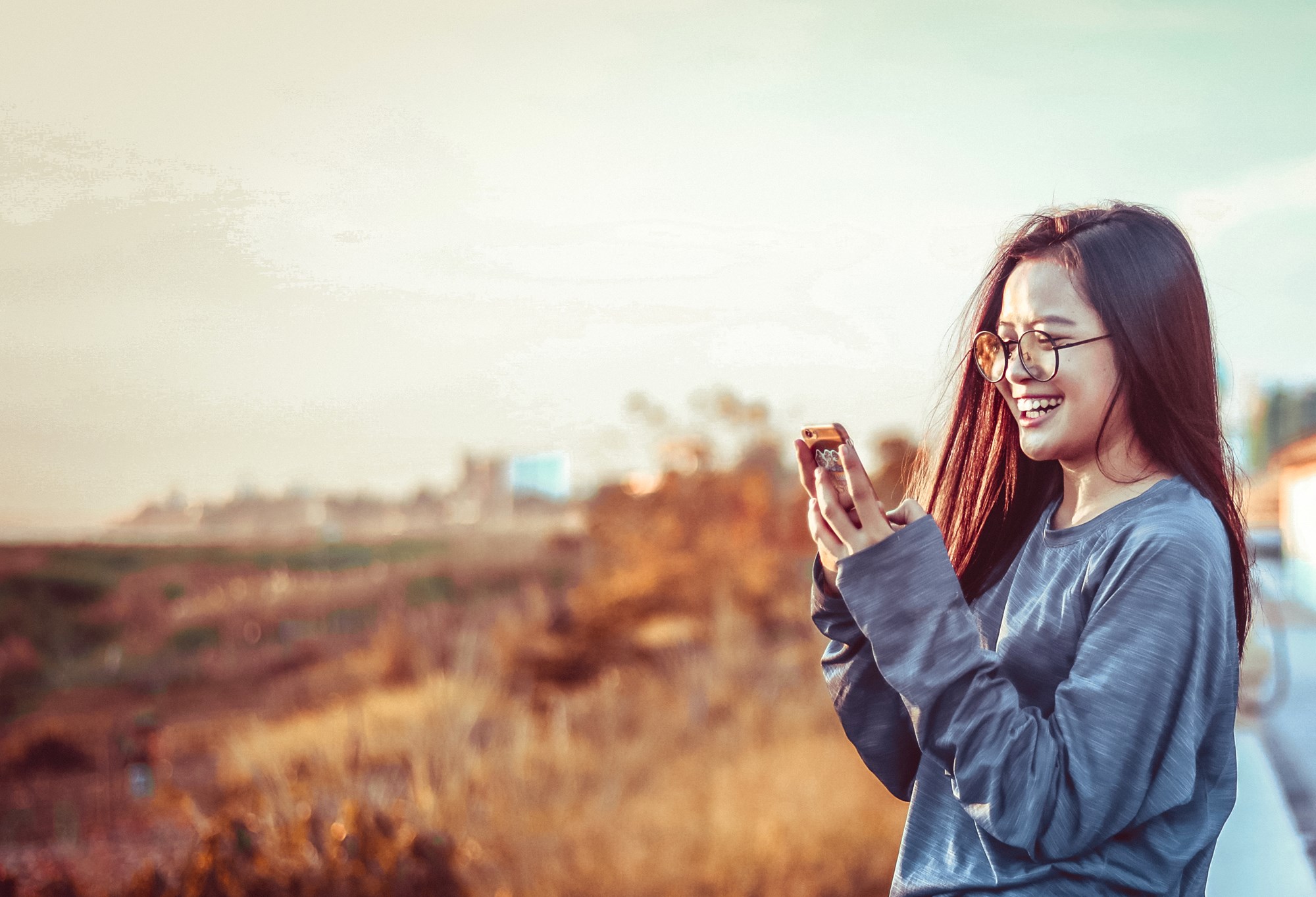 Young Teen Happily using Smartphone Texting at Outdoors