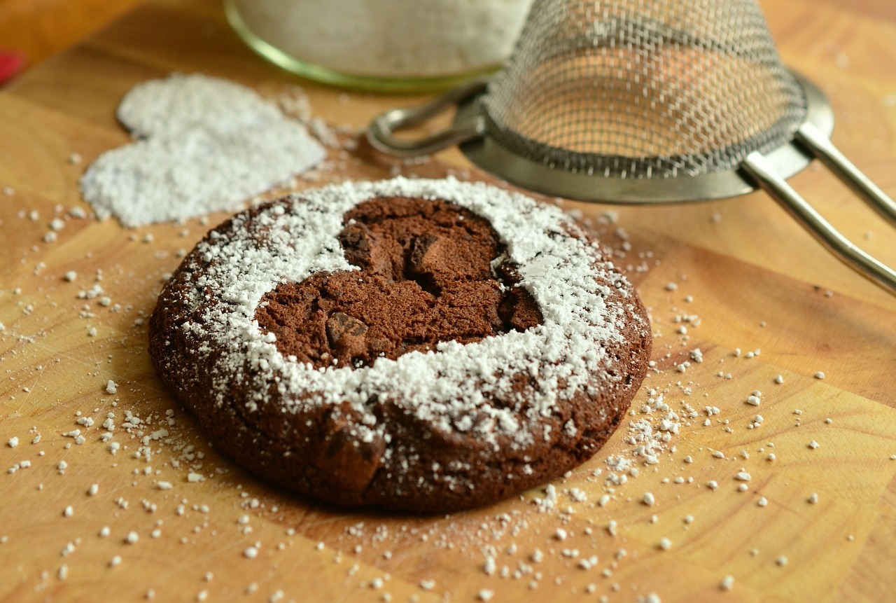 Picture of a chocolate cookie with a stencil of a heart on the top in powdered sugar.
