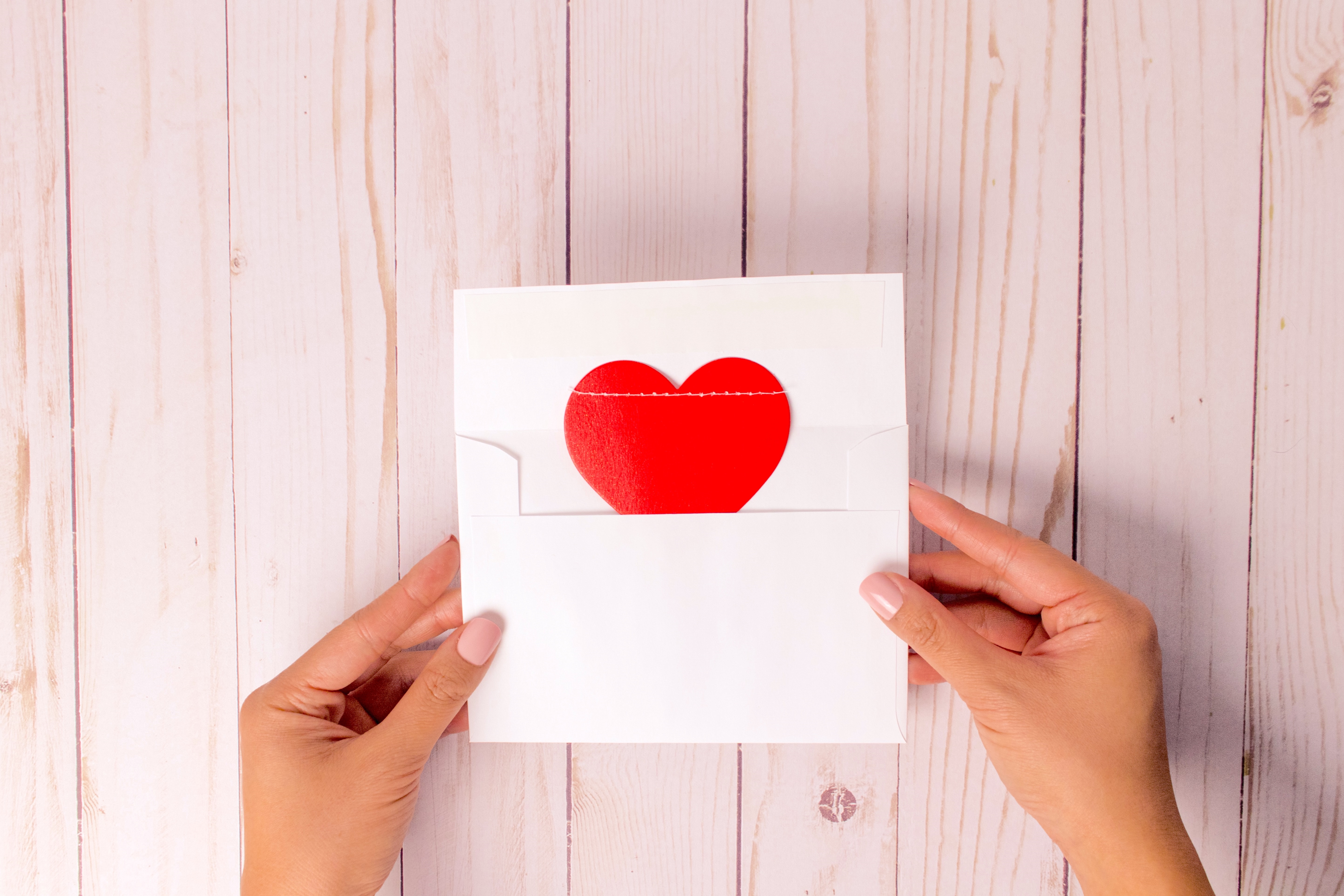 Picture of two female hands holding an envelope in which there is a piece of paper with a red heart.