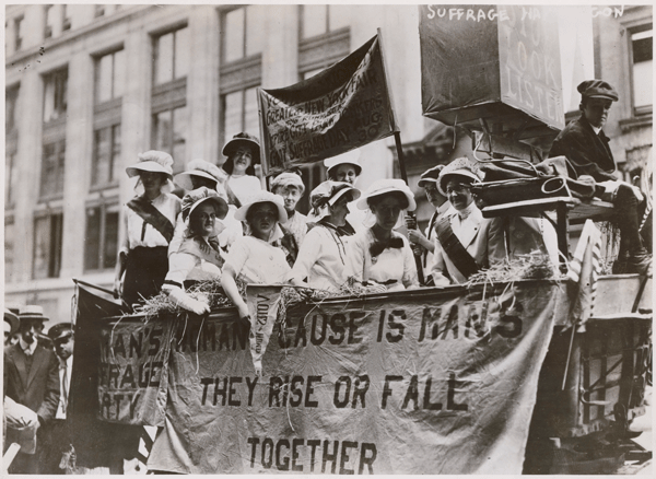Women on a suffrage parade float with banners advocating equal rights