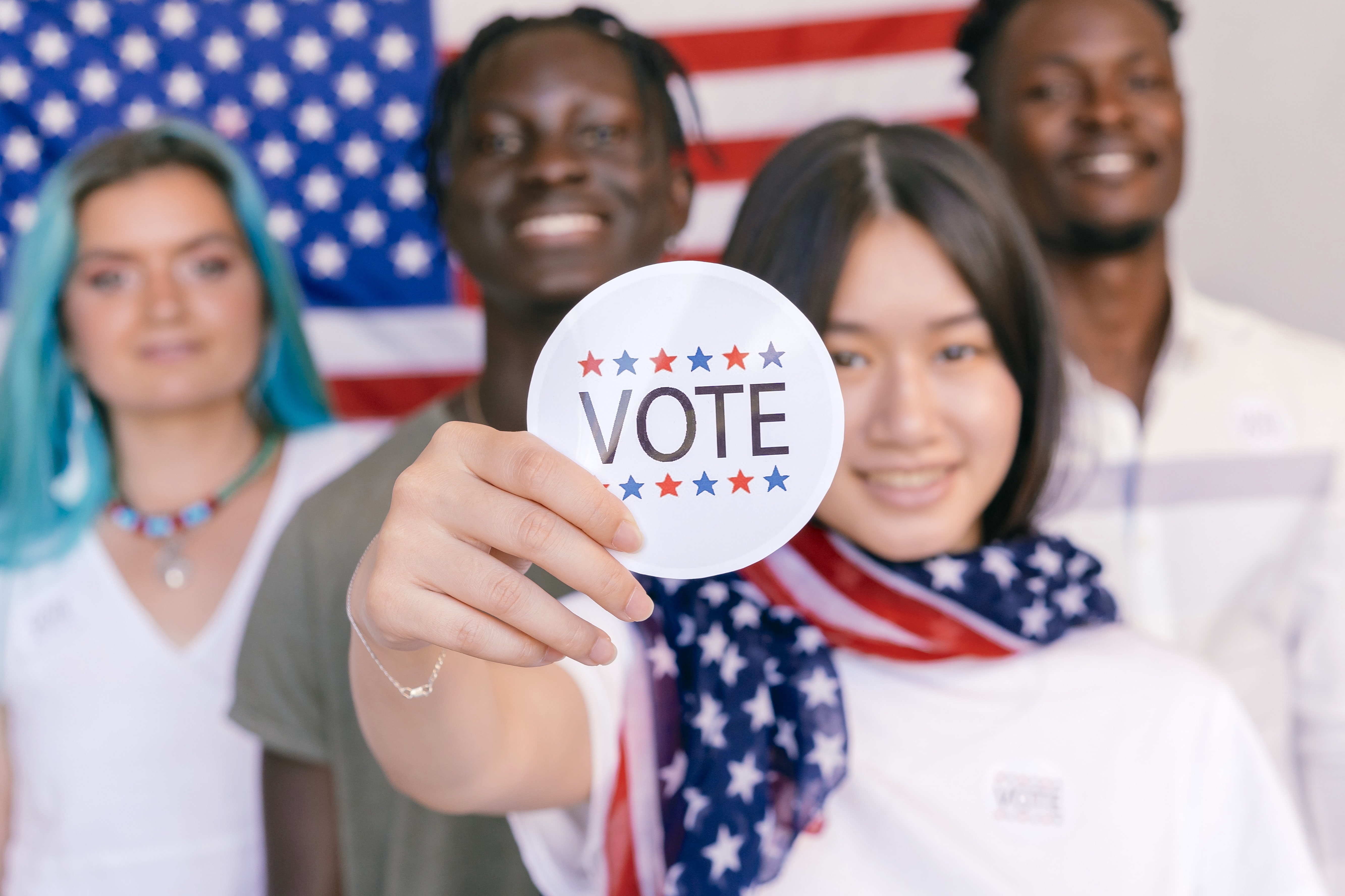 Voters standing in front of an American flag with one of them holding a Vote sign. 