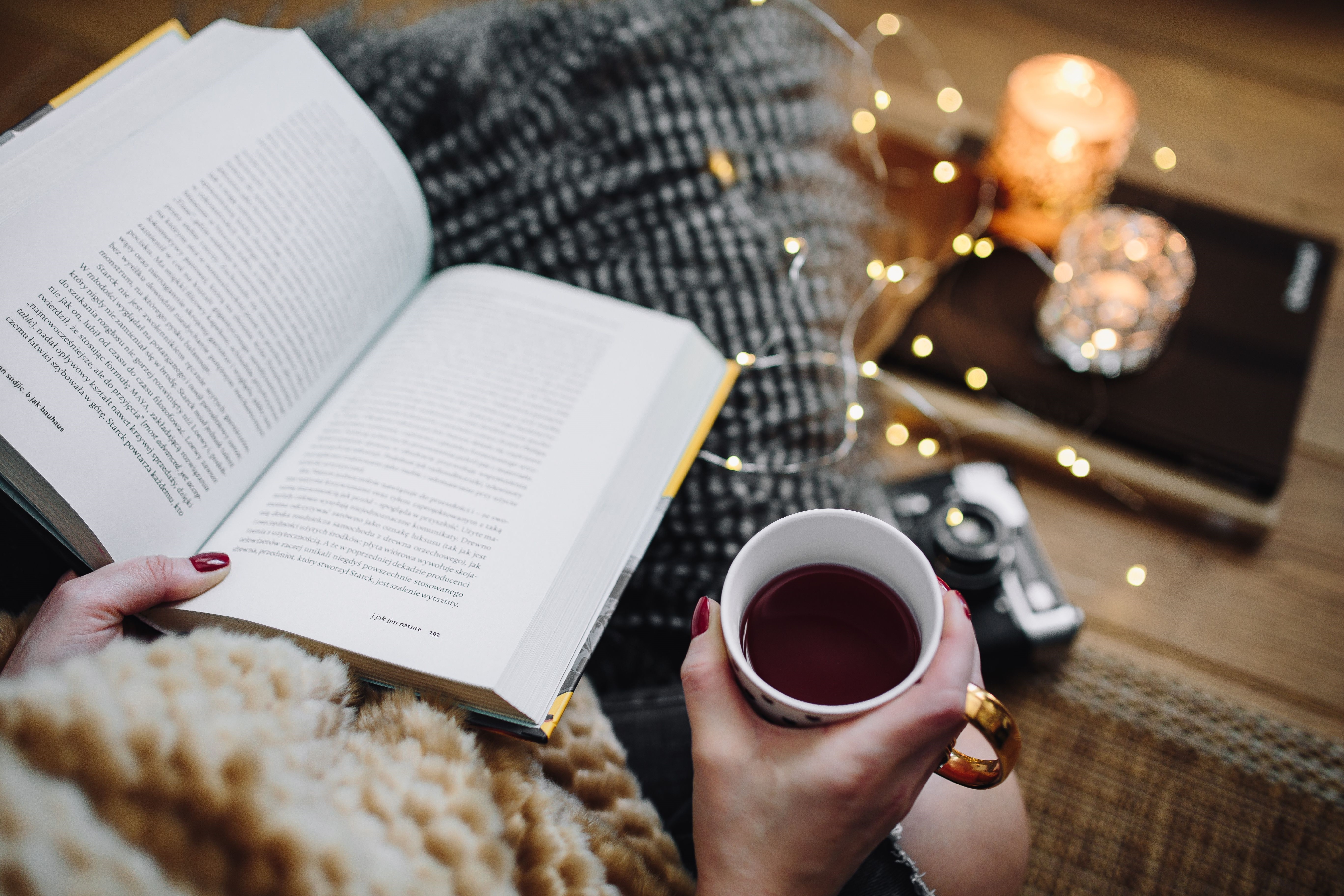 Woman Sitting in a Cozy Chair Reading a Book with a Cup of Tea