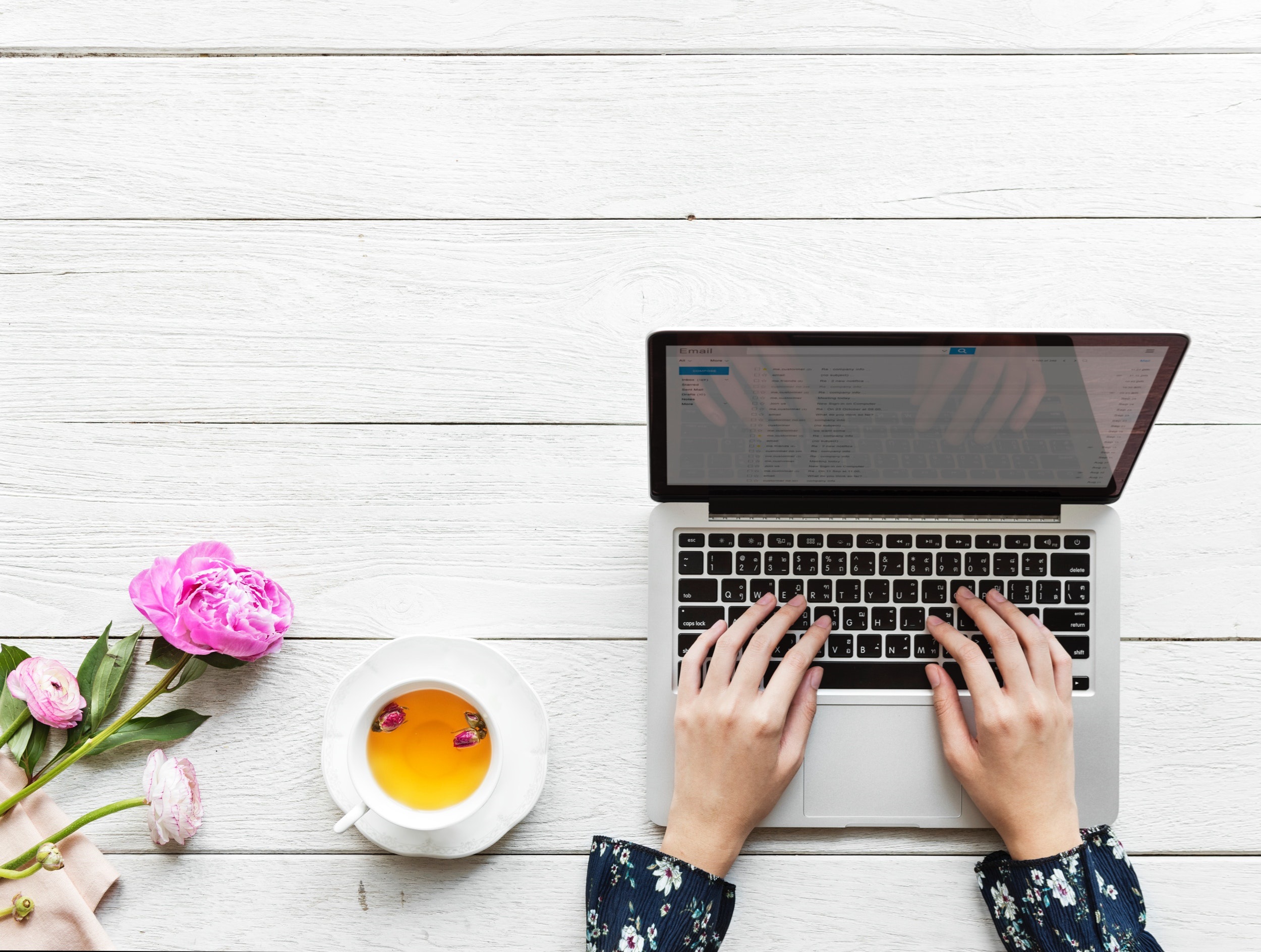 Closeup of Woman Working on Laptop With Coffee Cup and Flowers