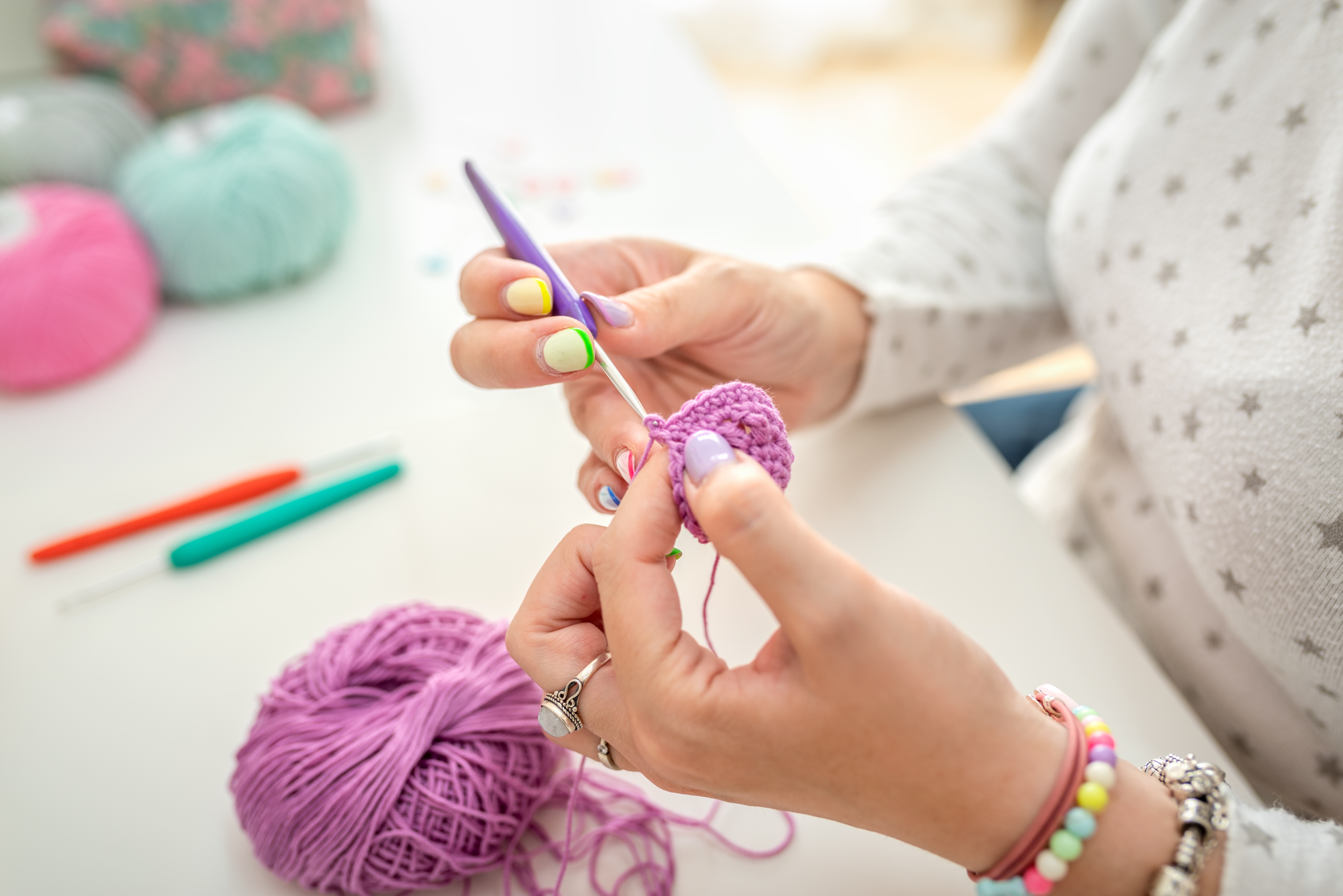 Close-Up Of Hands Crocheting With Purple Yarn In A Creative Workspace
