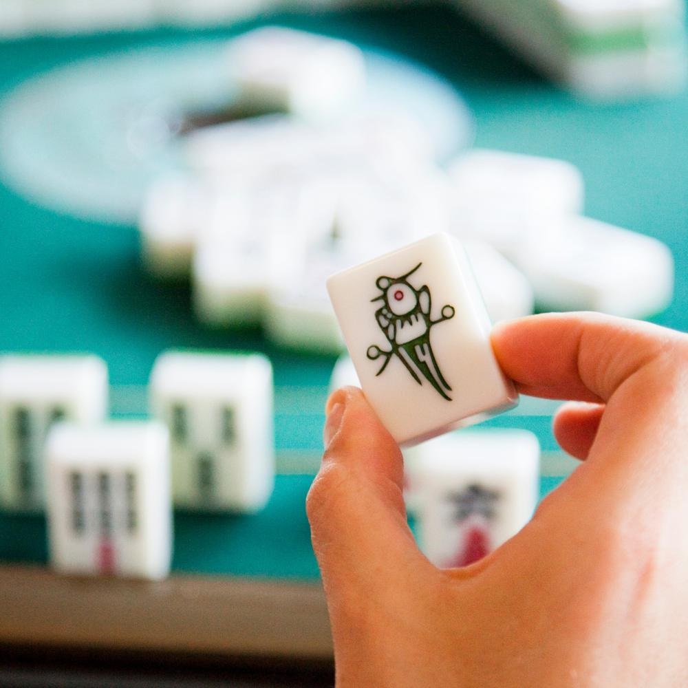 Up close view of a person's hand holding a Mahjong tile.