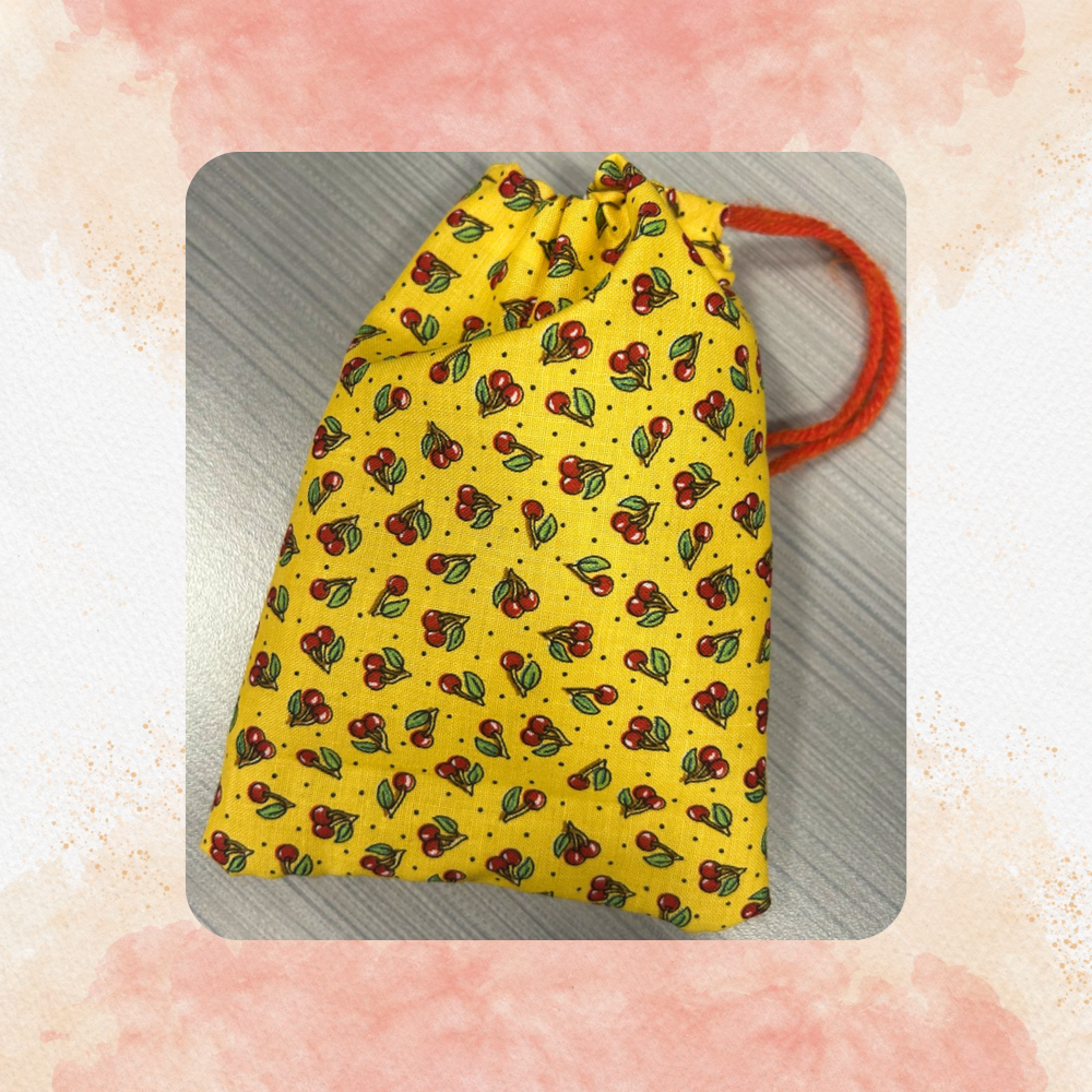 A yellow fabric pouch with a pattern of cherries and dots