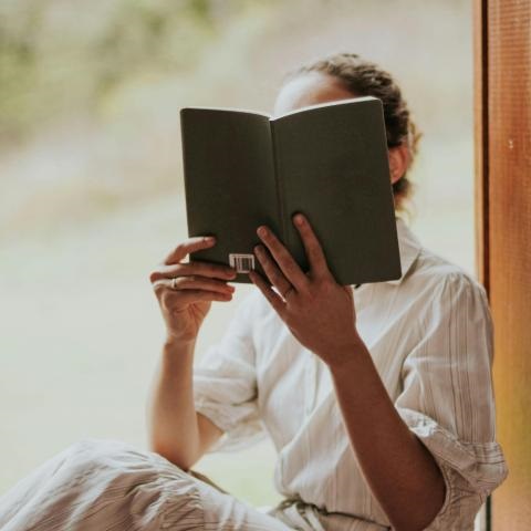 Women reading a book sitting near a window.