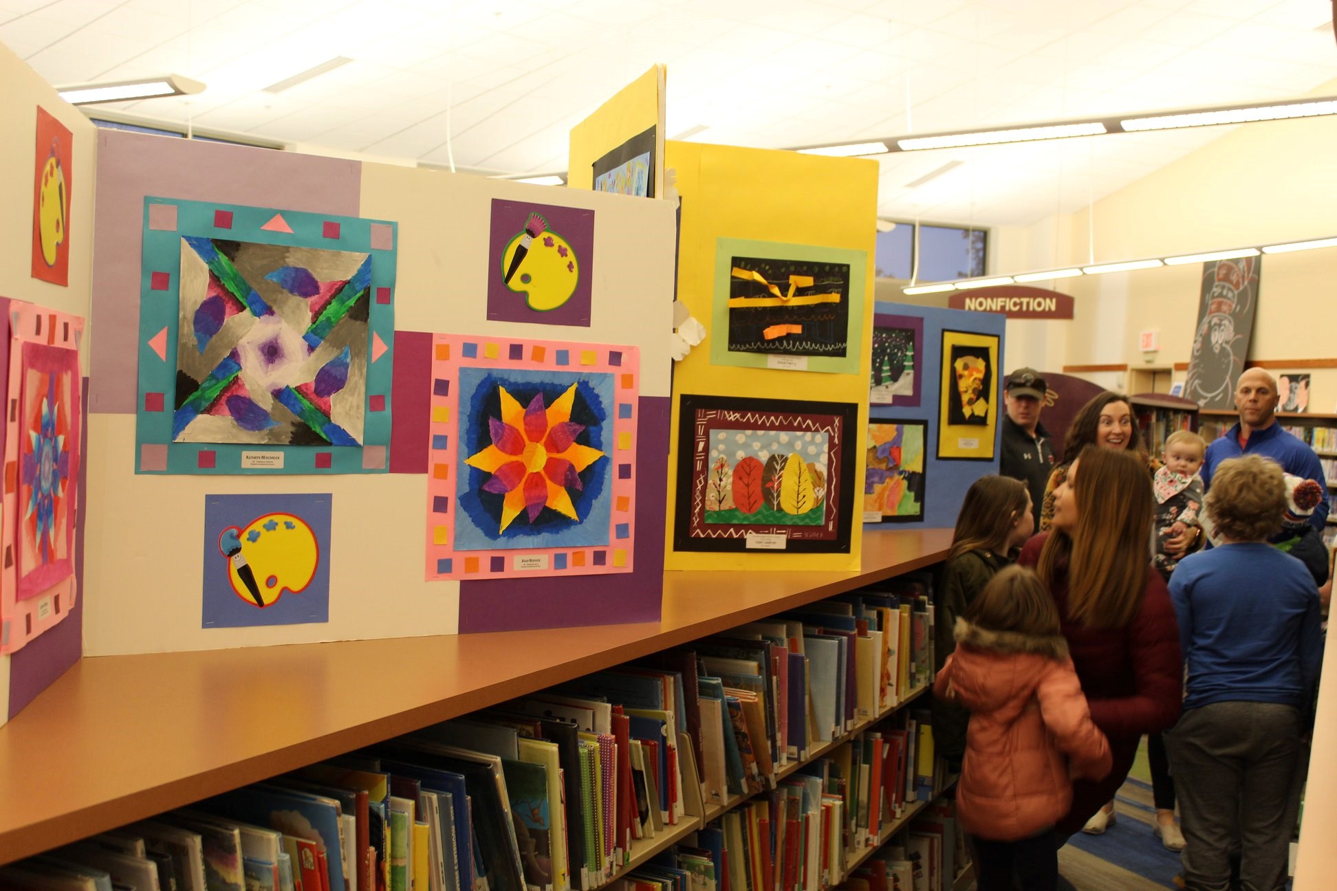 A picture of the children's area of the library as people look at displayed artwork.