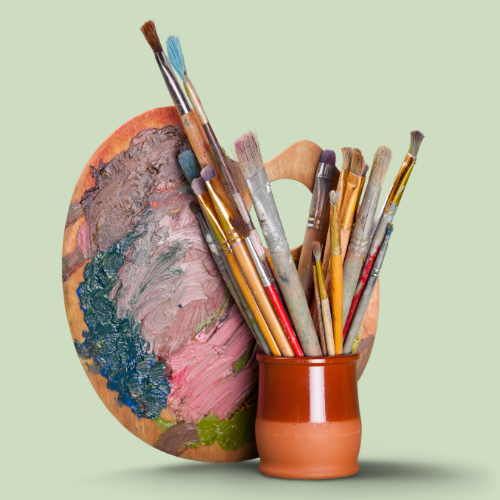 paint brushes in a vase in front of an artist paint palette on a light green background