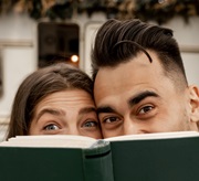 A smiling Hispanic man and woman read a book together at the library.
