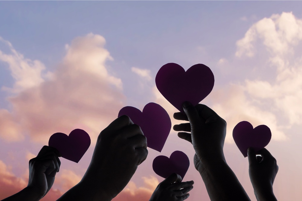 Hands holding paper hearts against a sky background