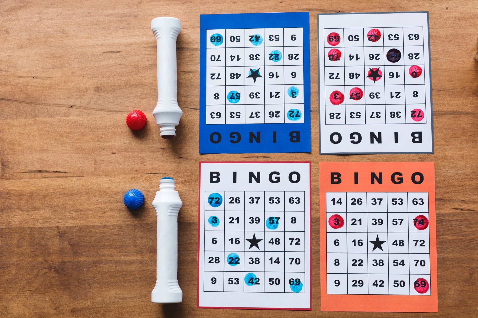 Four bingo game boards with two bingo dabbers sitting on a table.
