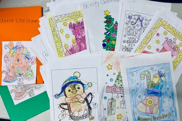 A pile of cards and coloring sheets with penguins, Christmas trees, and stockings on them, colored by the Girl Scouts and delivered to the Muskego Public Library for seniors.
