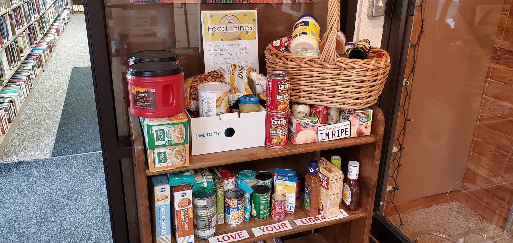 A brown wooden cart filled with non-perishable food items sits in the foyer of the Big Bend Village Library