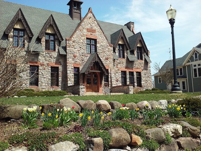 The L.D. Fargo Public Library, a large Gothic-style brick library building with pointed eaves. In front of the library is a small rock wall, tulips blooming, and a lamppost.