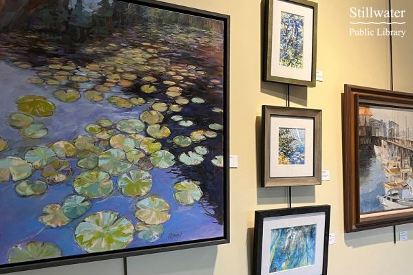Stillwater Public Library's gallery wall with 5 pictures painted by Marianne Barratt; Featured large painting of lily pads on water