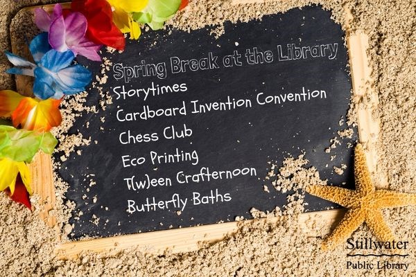 Small black chalkboard buried in sand with starfish on right and lei on left