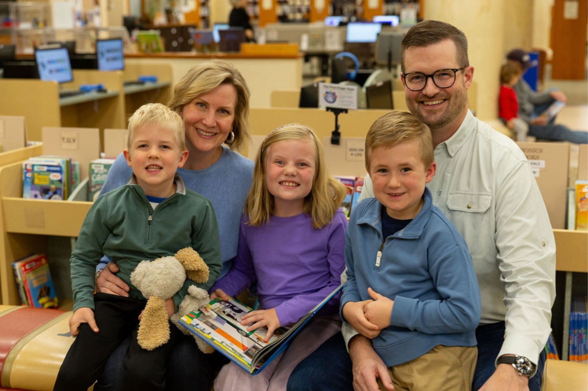 Parents with three children sitting on bench in library and reading
