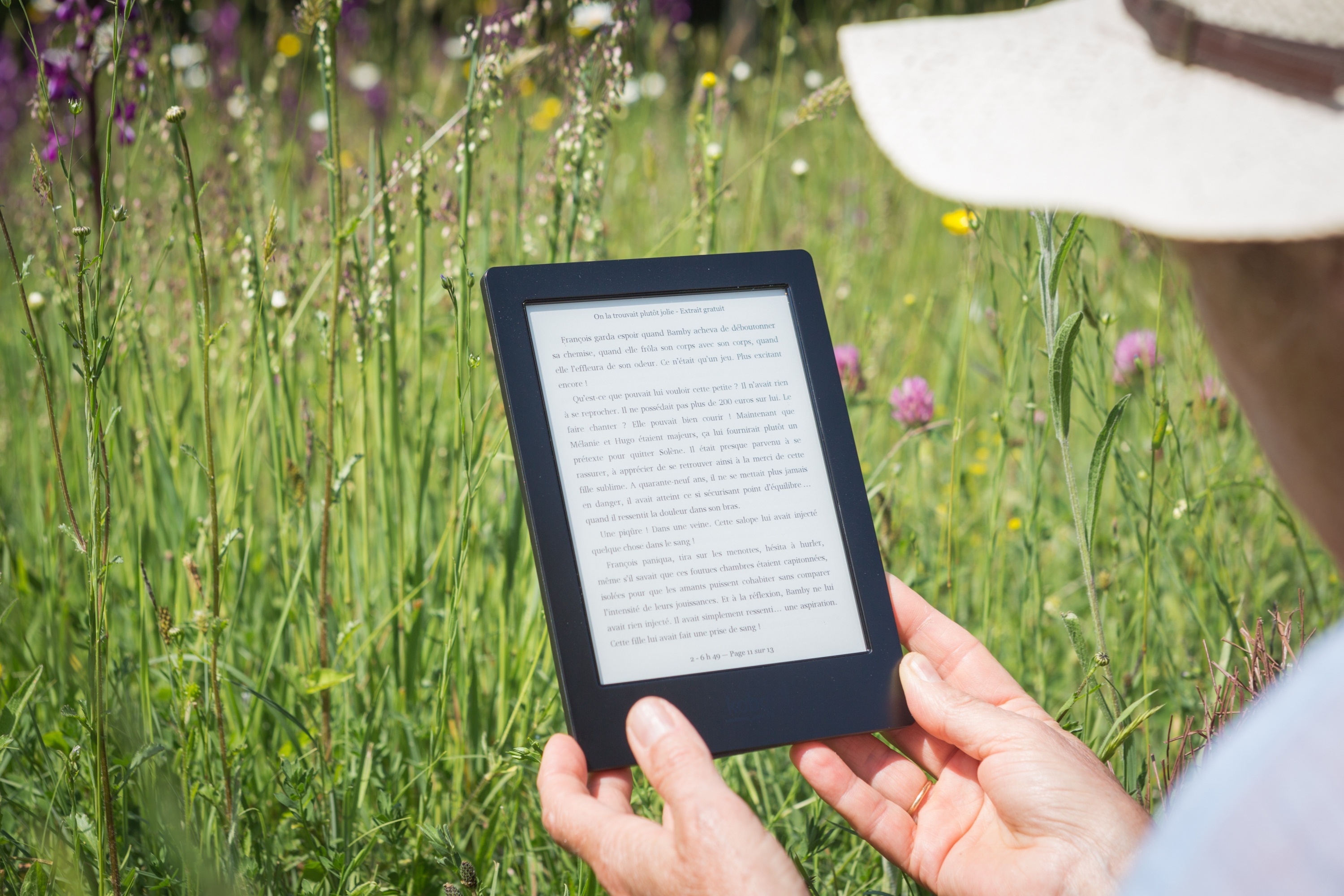 Image by Capucine from Pixabay View over someone's shoulder reading an audiobook on an e-reader with a meadow of flowers in the background.