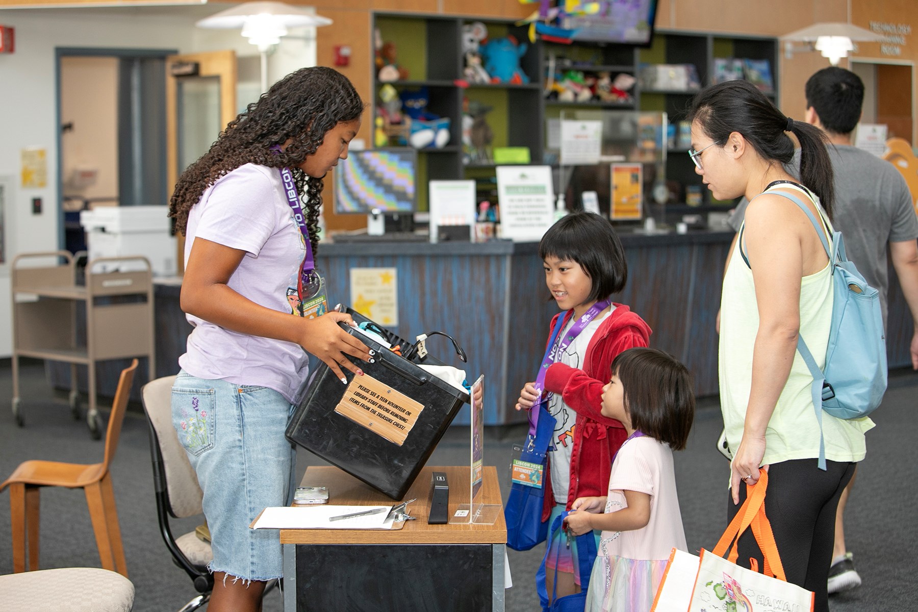 Teen volunteer shows summer reading prizes to kids.
