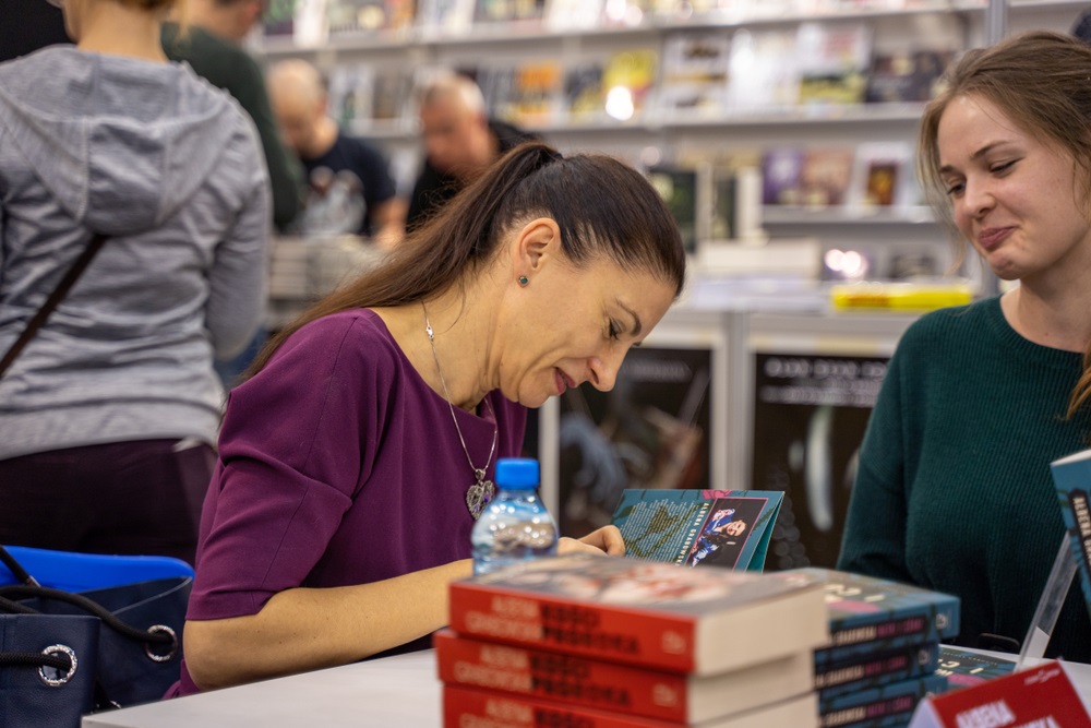author sitting at table signing book as fan looks on