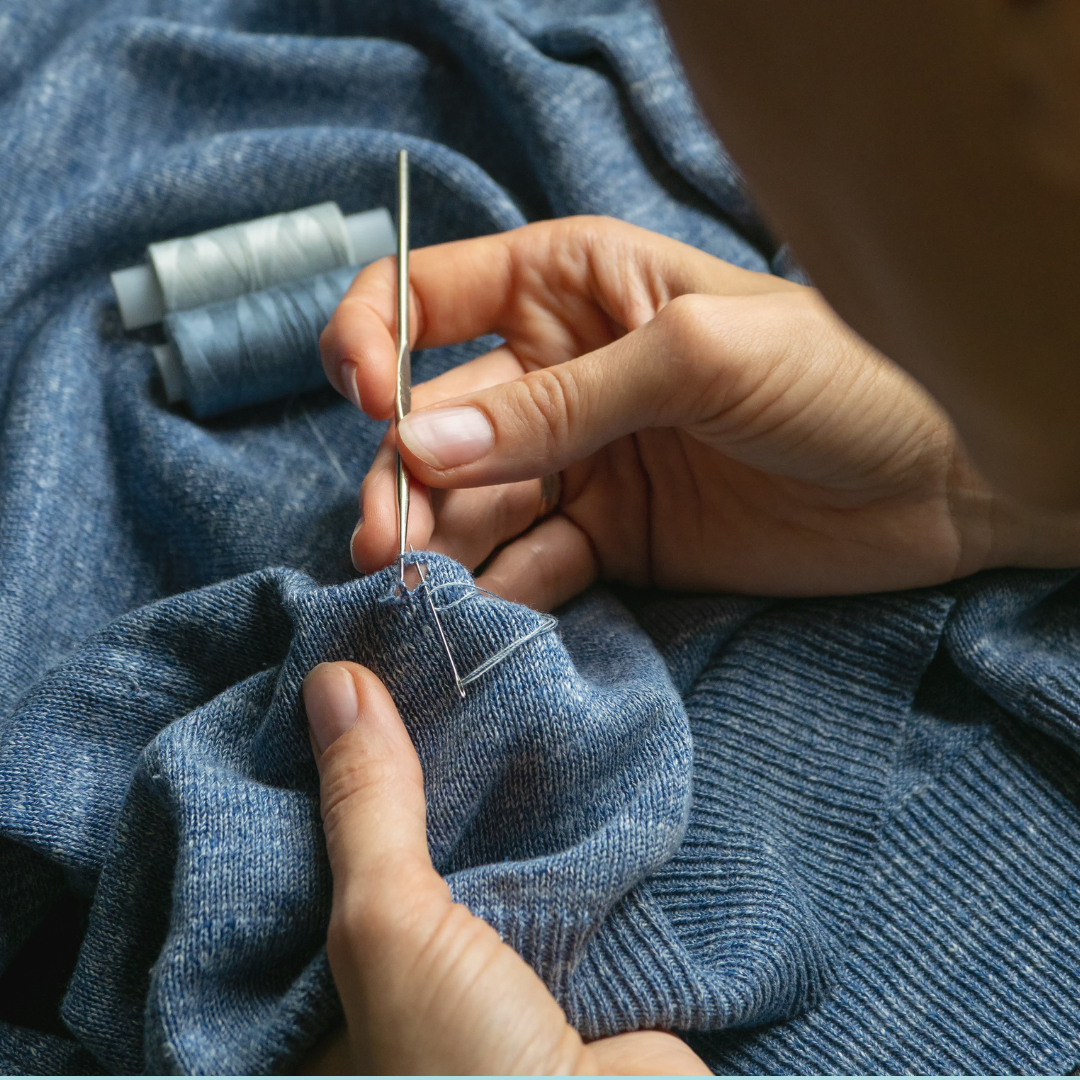 Someone holds a needle and repairs a blue sweater with a hole