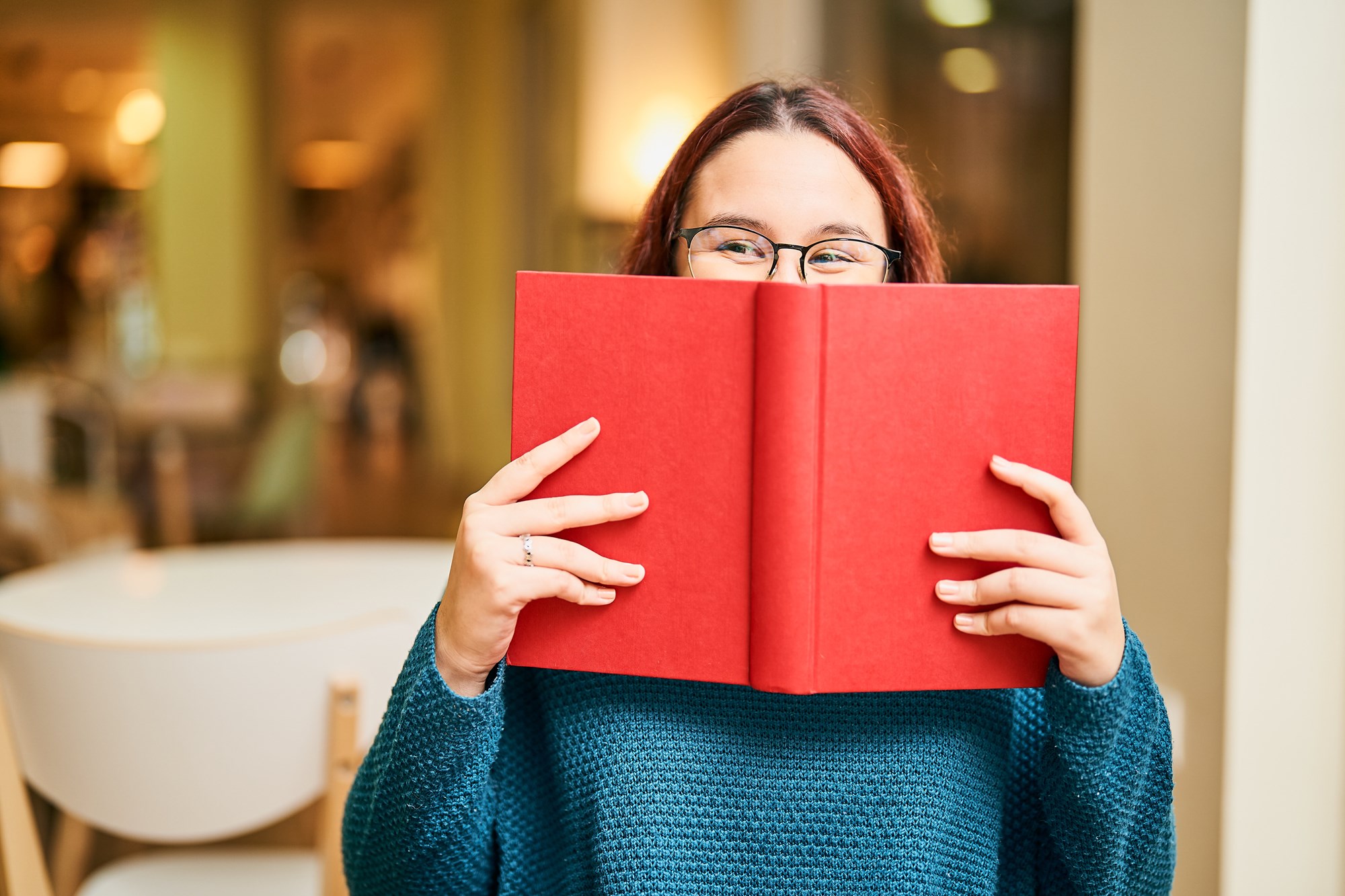 Young Woman Hiding Her Face Behind A Red Book And Smiling Young Woman Hiding Her Face Behind A Red Book And Smiling