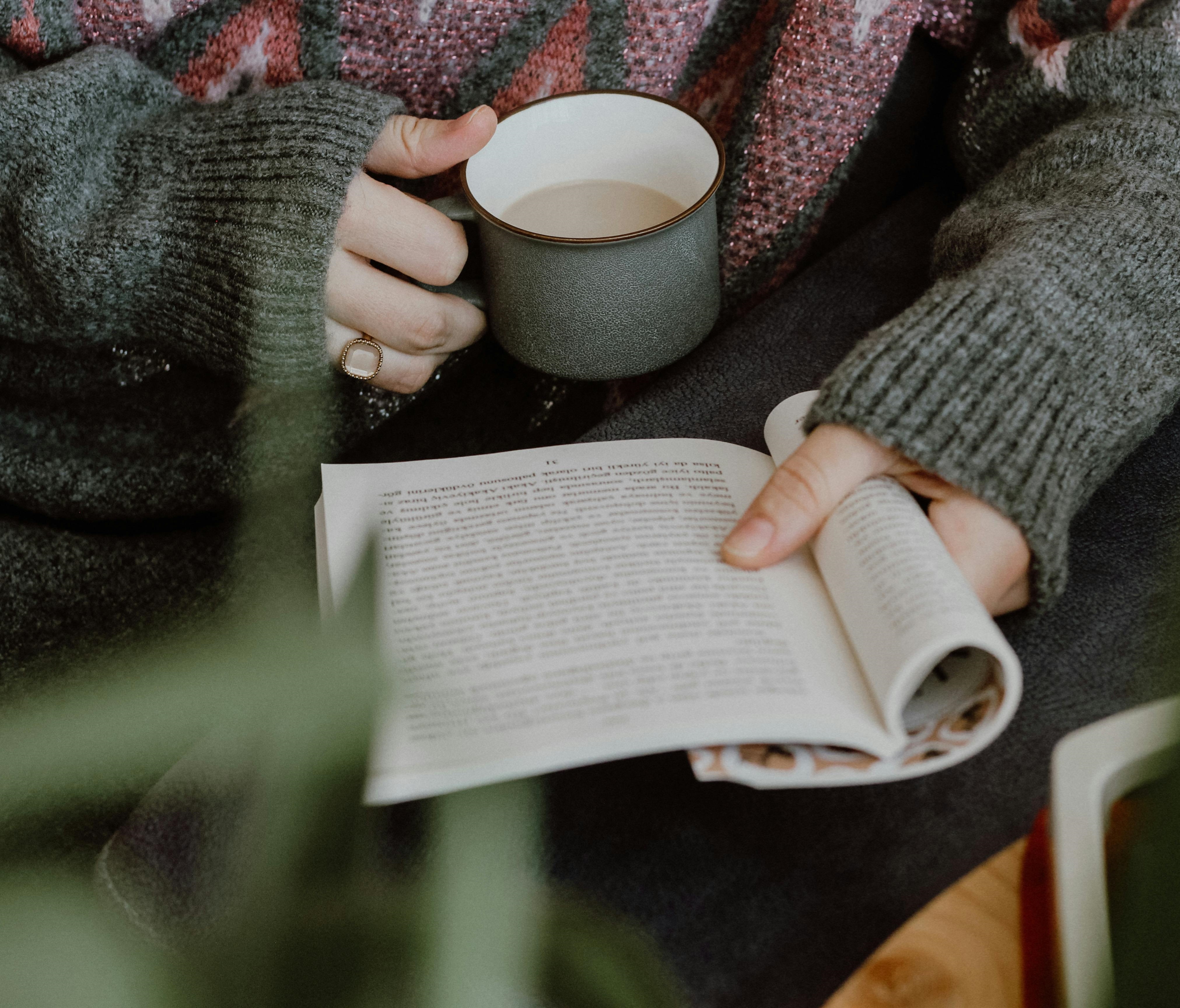 Person Holding an Open Book and Mug of Coffee