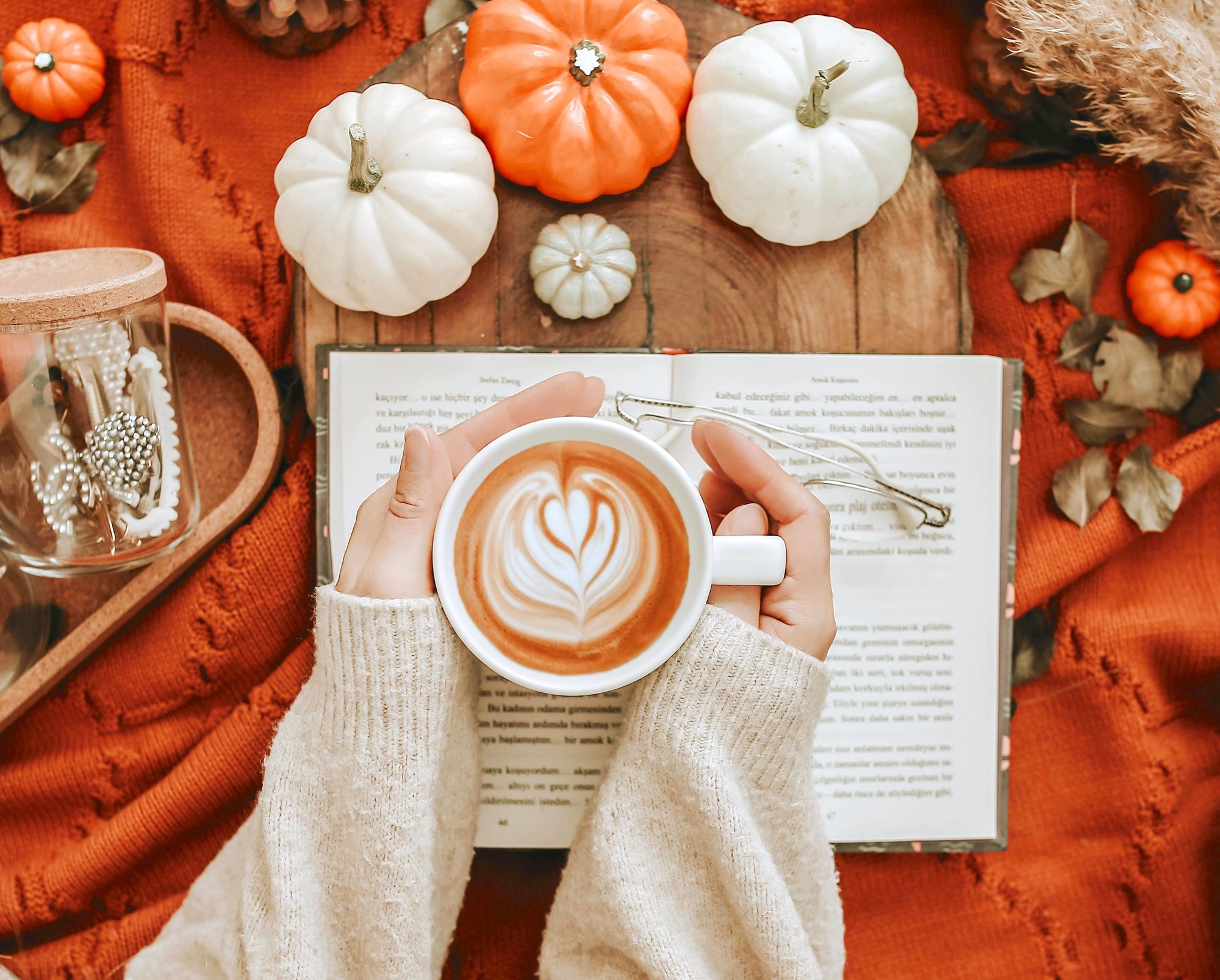 Person Holding a Coffee Mug Over an Open Book in a Fall ScenePumpkins