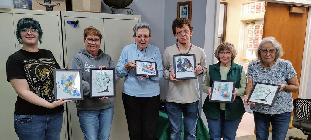 Participants in the library's creative outlet class holding their framed art work 
