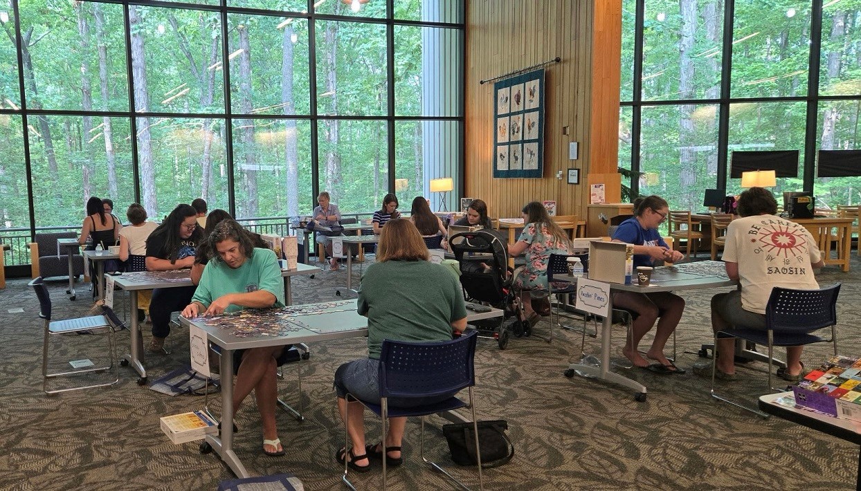 People sitting at tables in a library working as teams on solving jigsaw puzzles