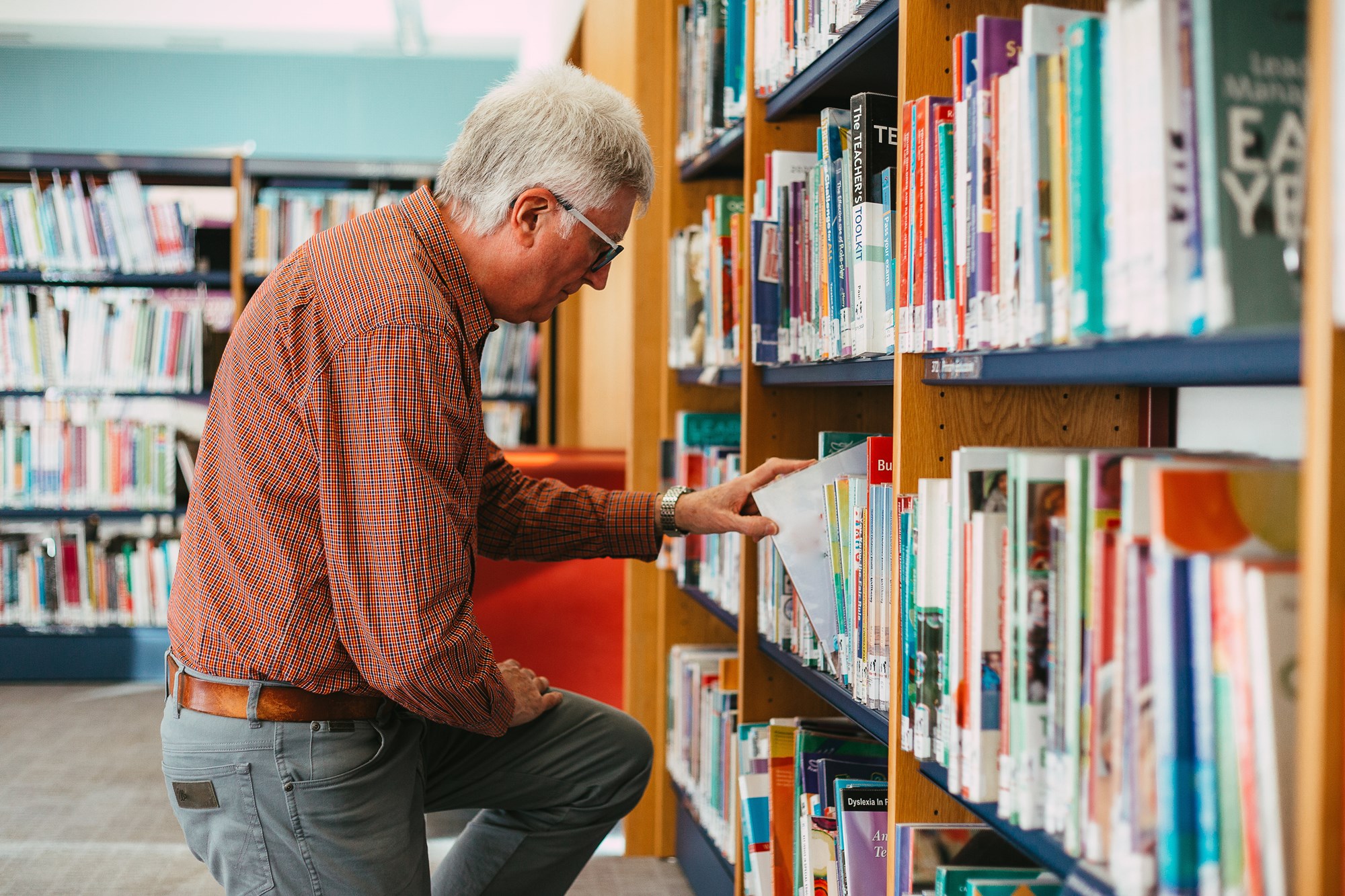 Senior Man Looking at Books on Shelf in Library