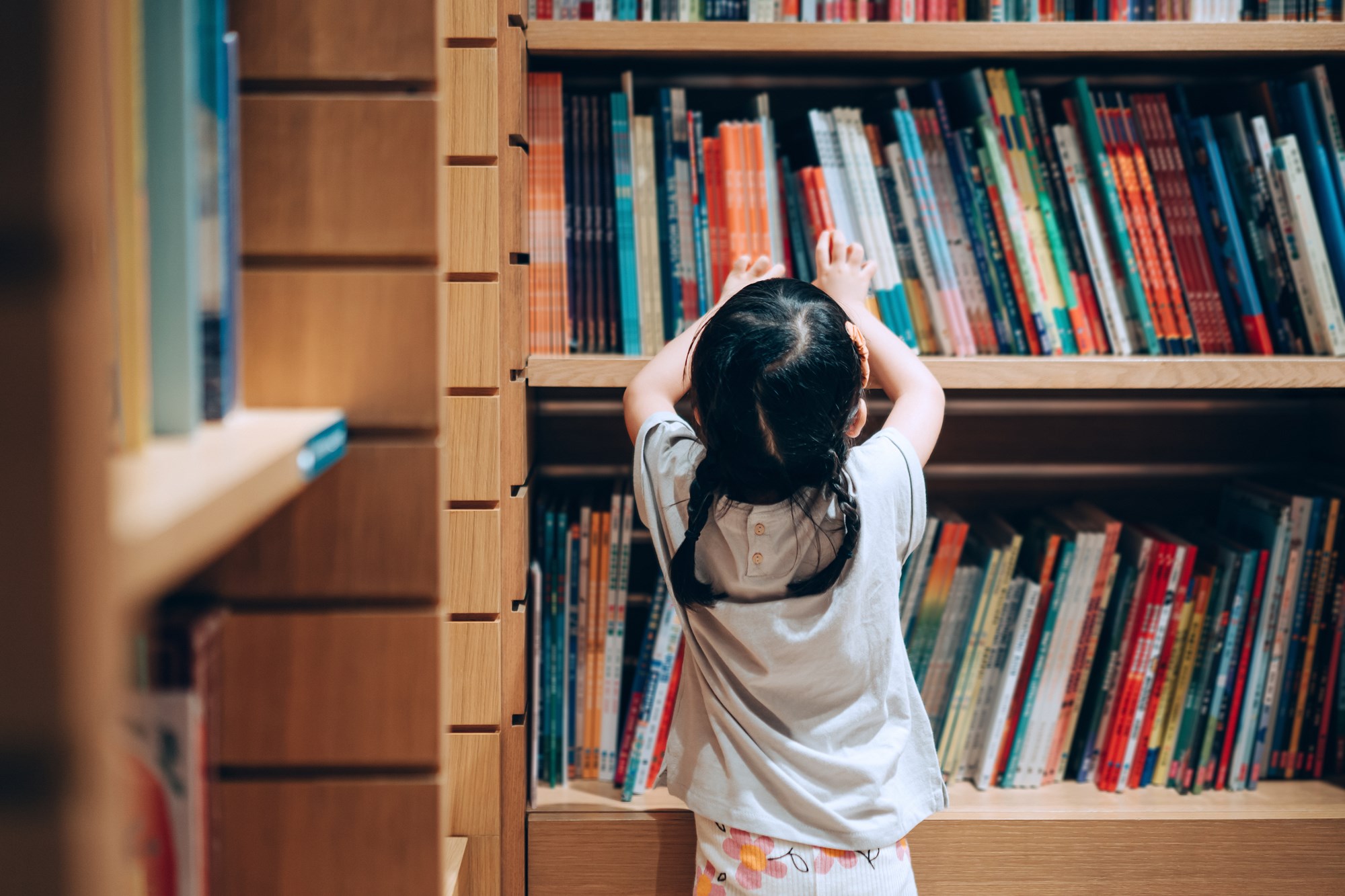Little Girl Choosing Books from the Bookshelf in Library