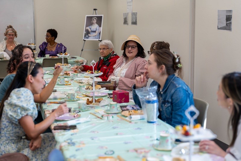 Women sitting at a tea party, some in Regency-era costumes