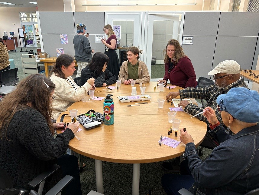Mixed age group of people sitting around a library table mixing scents to make perfume