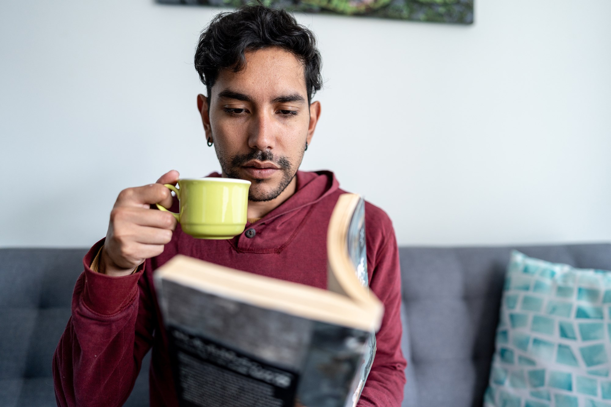 Young Man Reading a Book and Drinking Coffee at Home