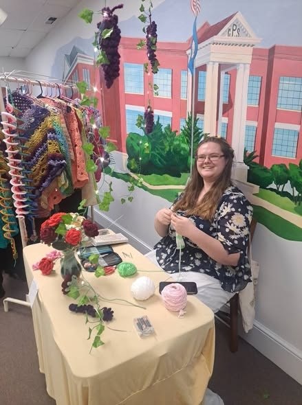 smiling woman sitting at a table knitting