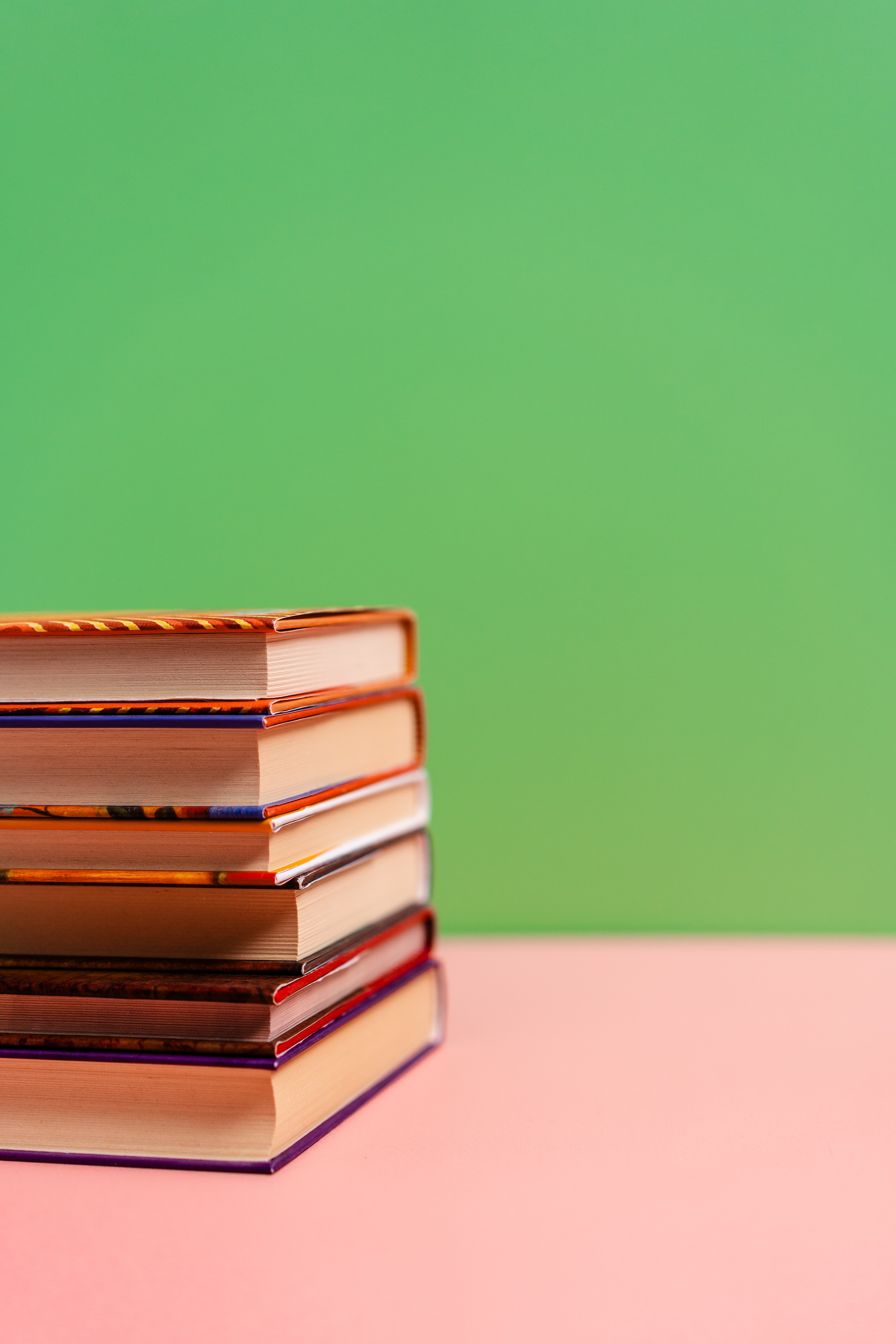 Stack of Books on the Table Against a Plain Green and Pink Background