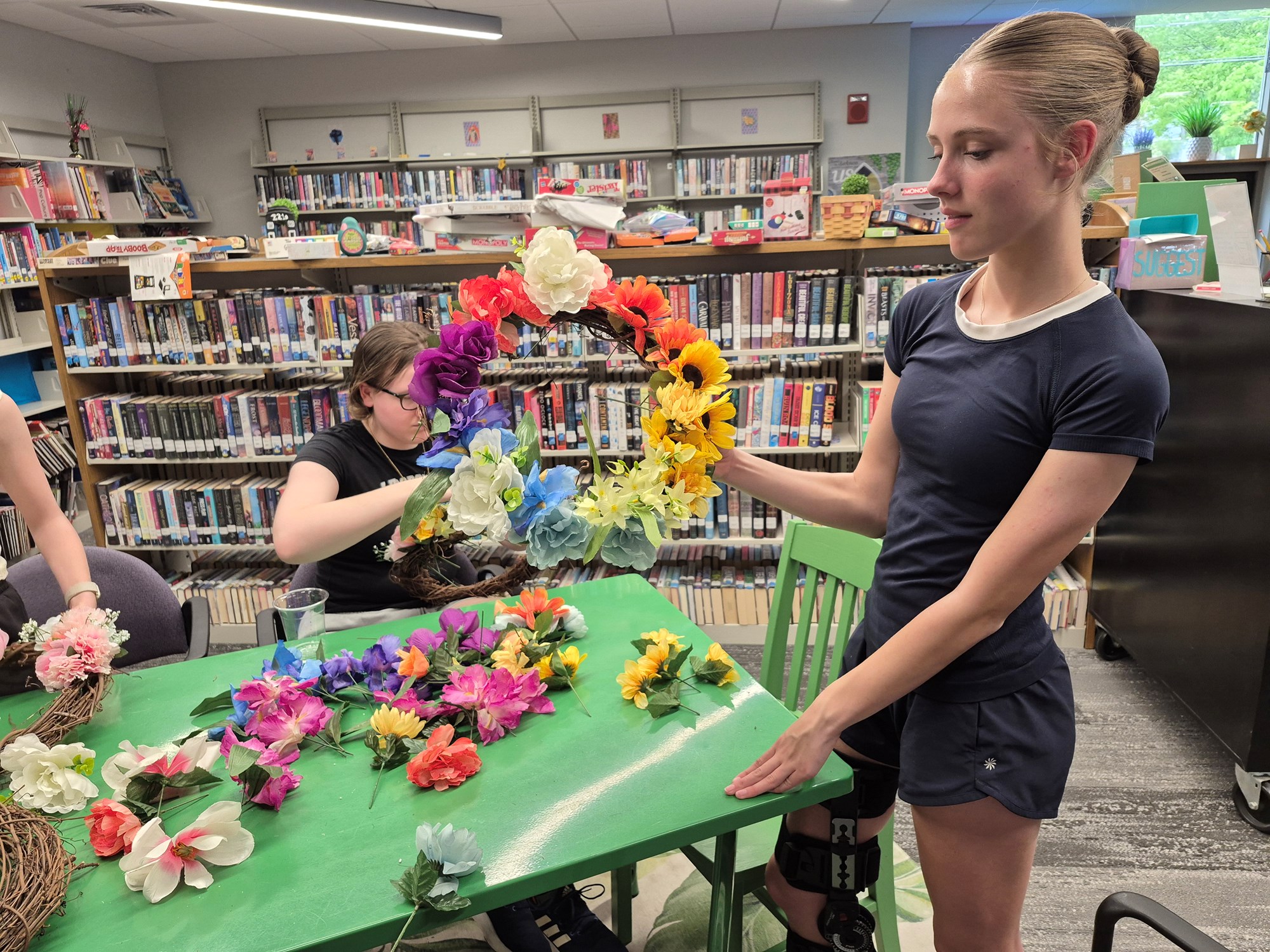 A teen holding up a completed rainbow flower wreath in the Teen Scene.