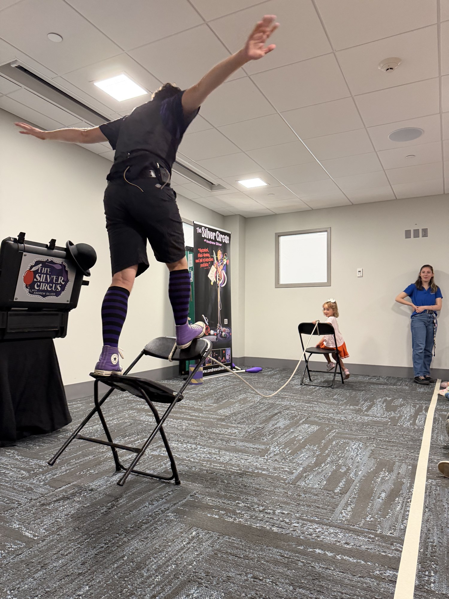 A member of Silver Circus Variety Show balancing on a chair in the Meeting Room.