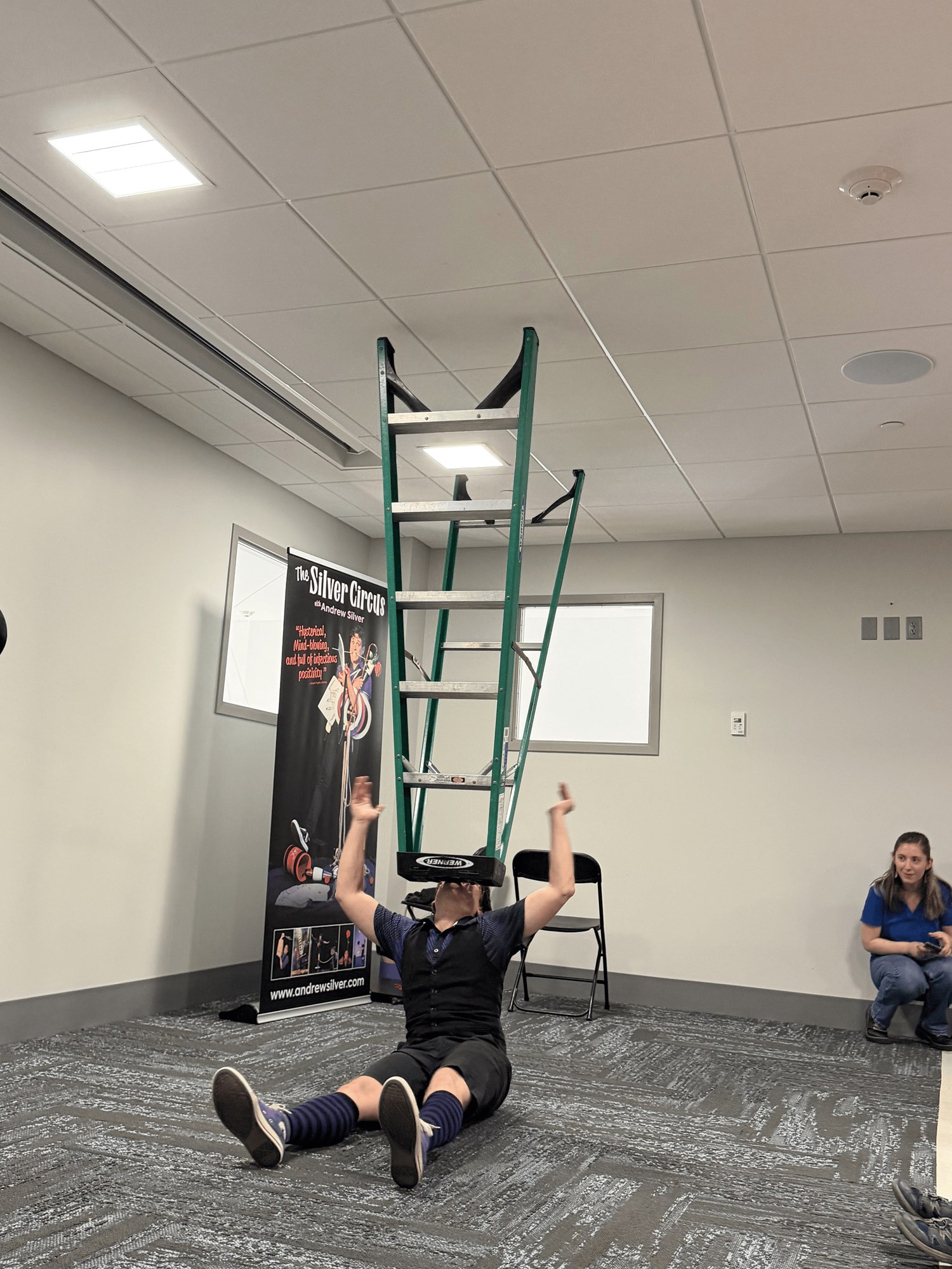 A member of Silver Circus Variety Show balancing a ladder on his head in the Meeting Room.