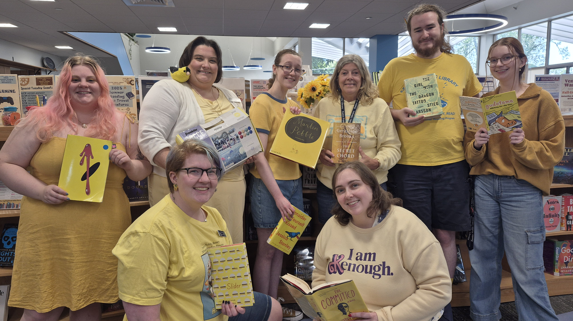 Staff members wearing various shades of yellow standing in front of the new shelf on the main floor of the library. Staff members wearing various shades of yellow standing in front of the new shelf on the main floor of the library.