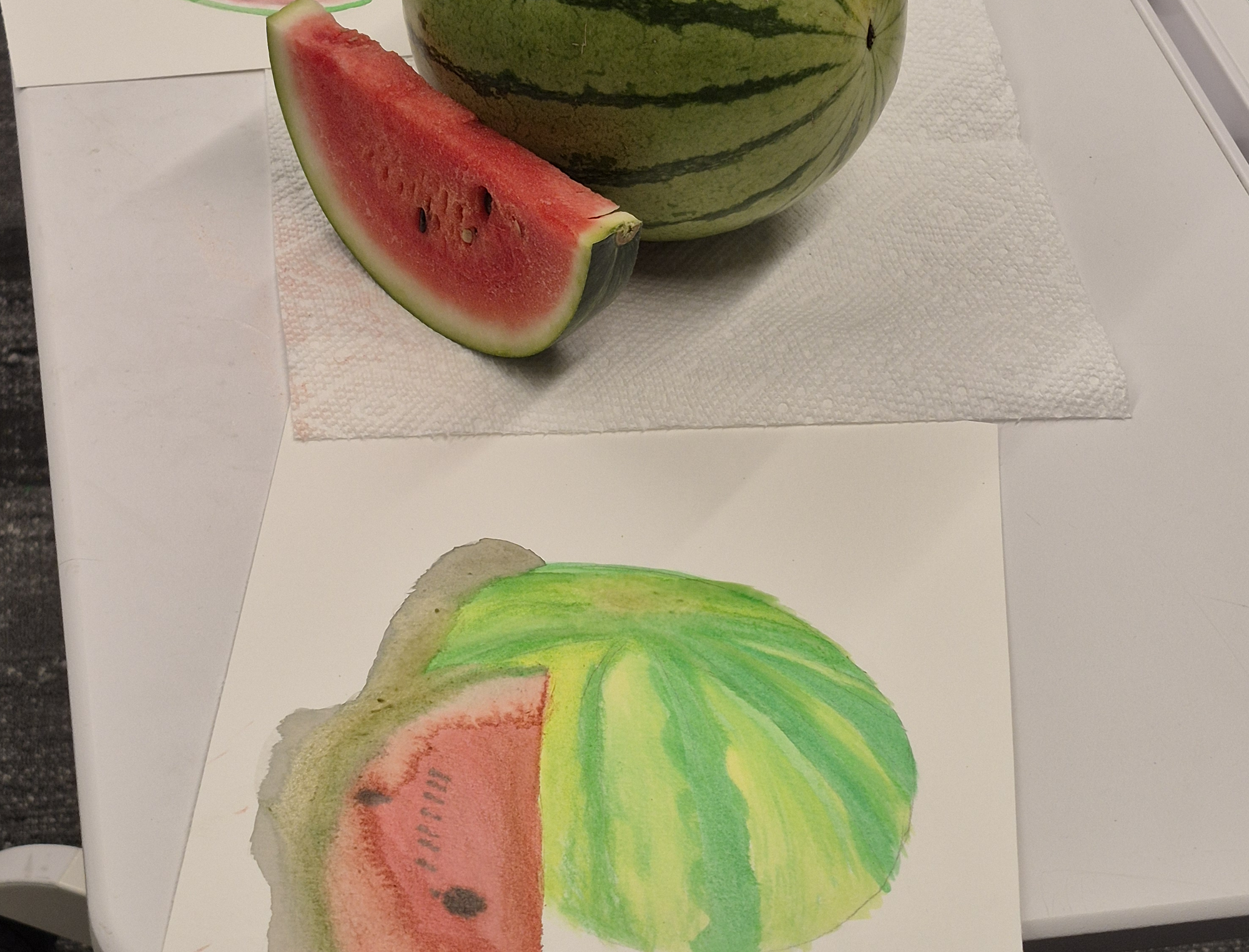 Close up of the watermelon and watermelon slice with one of the paintings in front of it.
