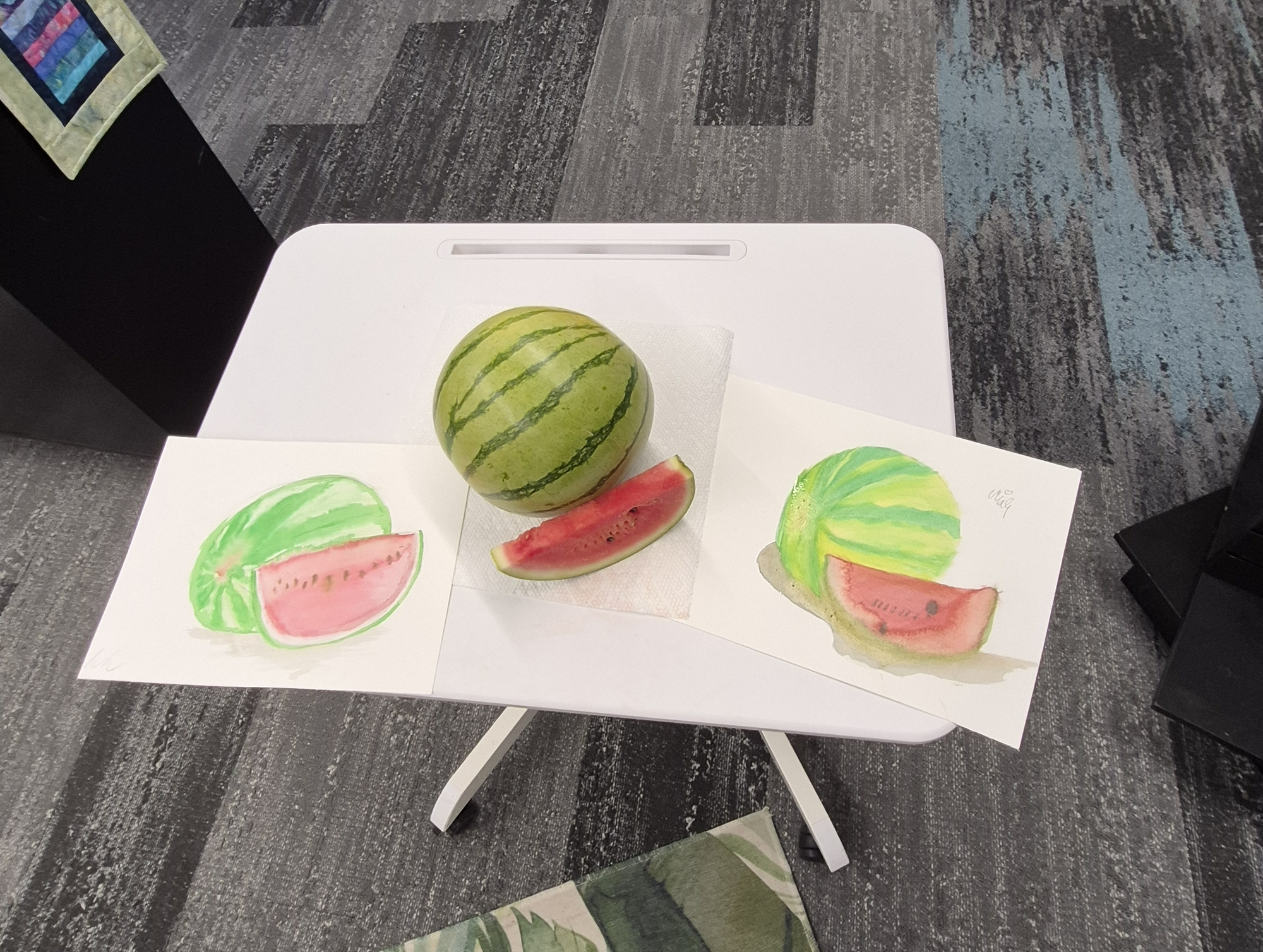 A whole watermelon plus a slice with two watercolor paintings next to it.