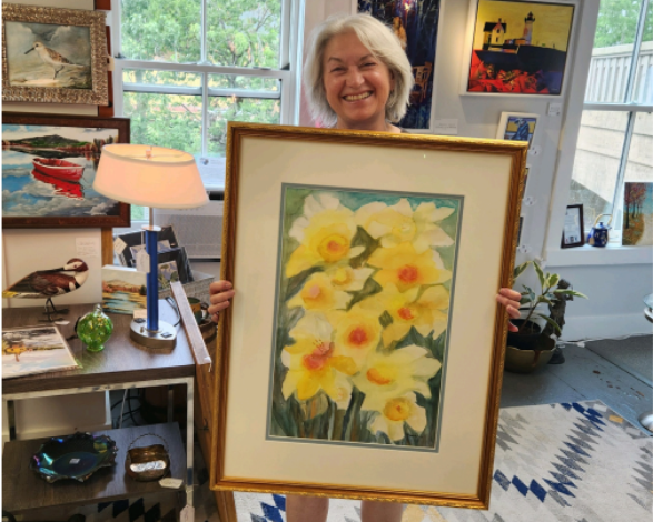 December artist K.A. Lawrence/Flygare holding up a watercolor painting of yellow flowers on a green background.
