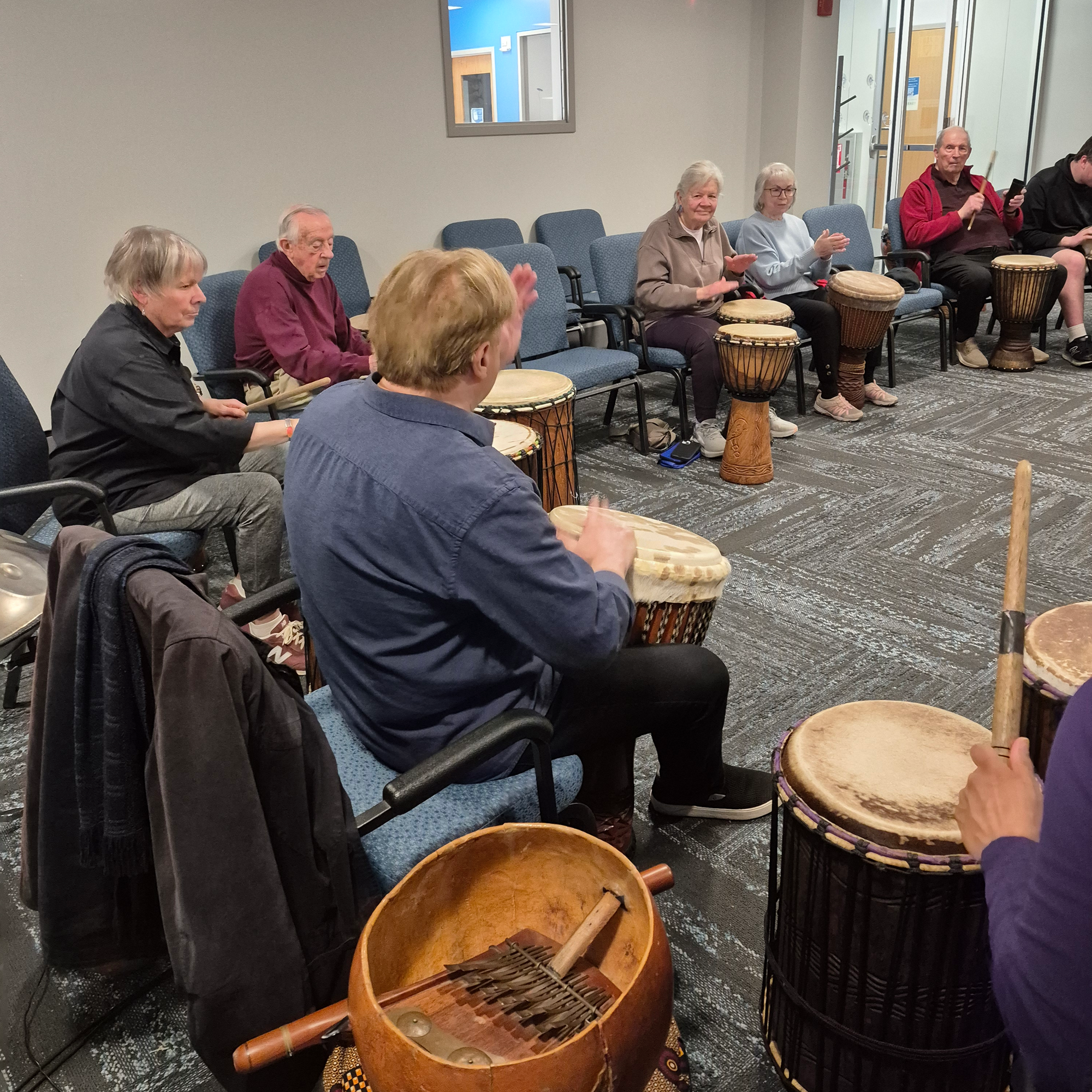 Close up of Randy Armstrong and patrons playing drums in the Meeting Room.