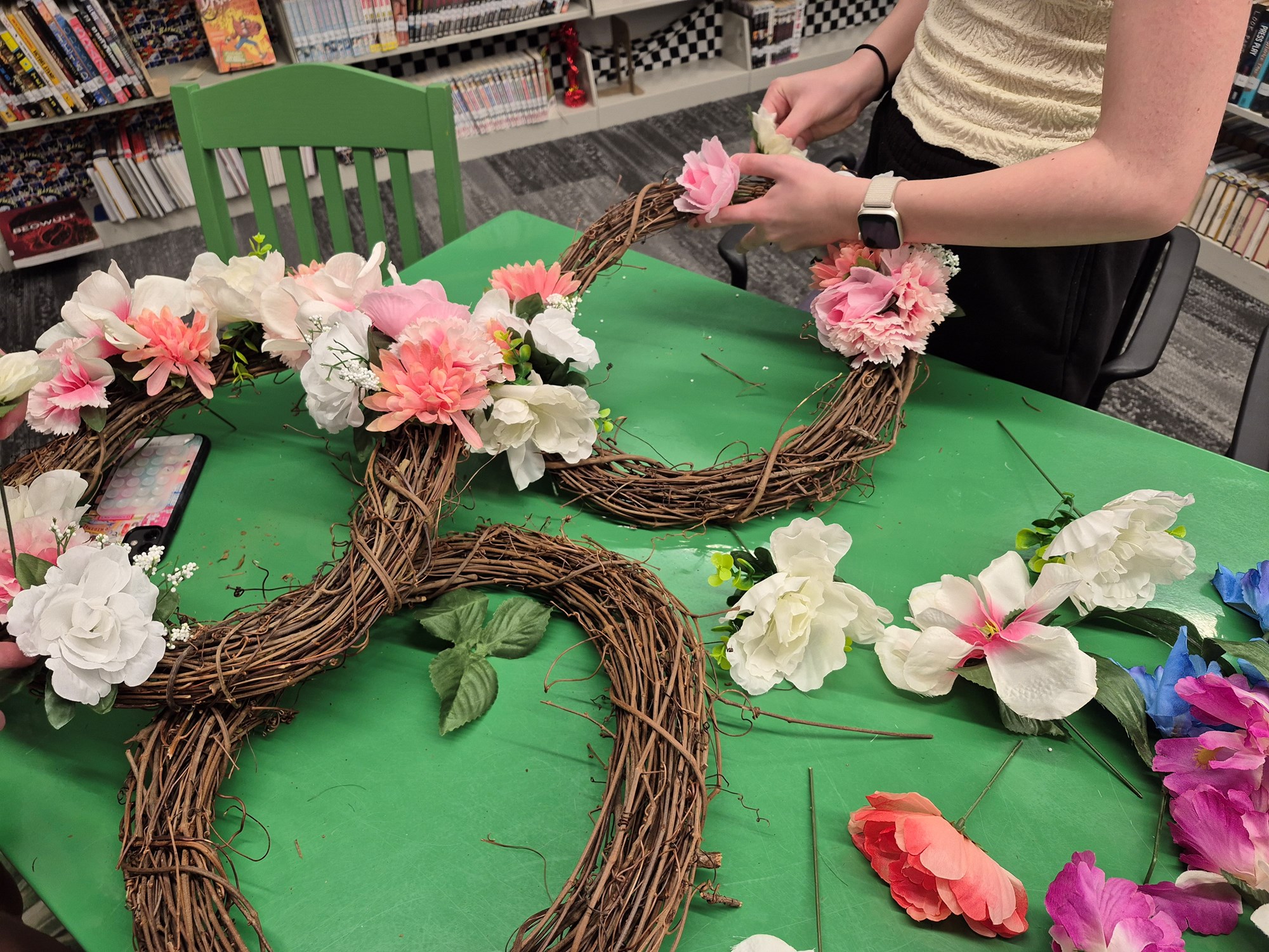 Flower wreaths with white, pale pink, and deeper pink flowers on a green table in the Teen Scene.